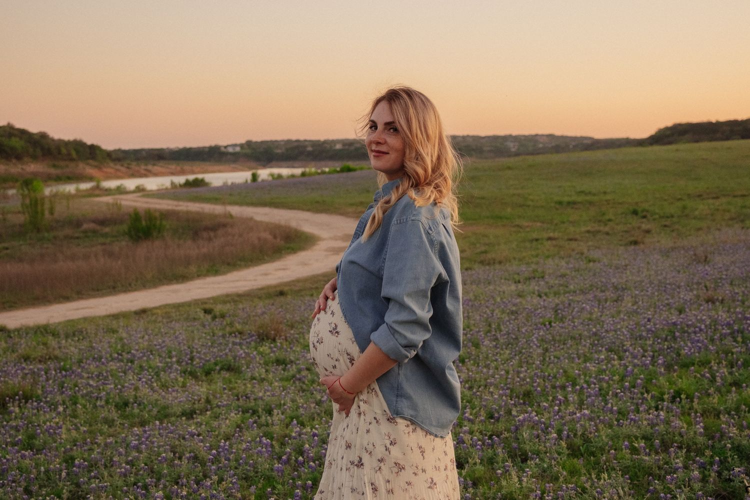 Person in denim jacket walks along winding path through blooming wildflower field at sunset.