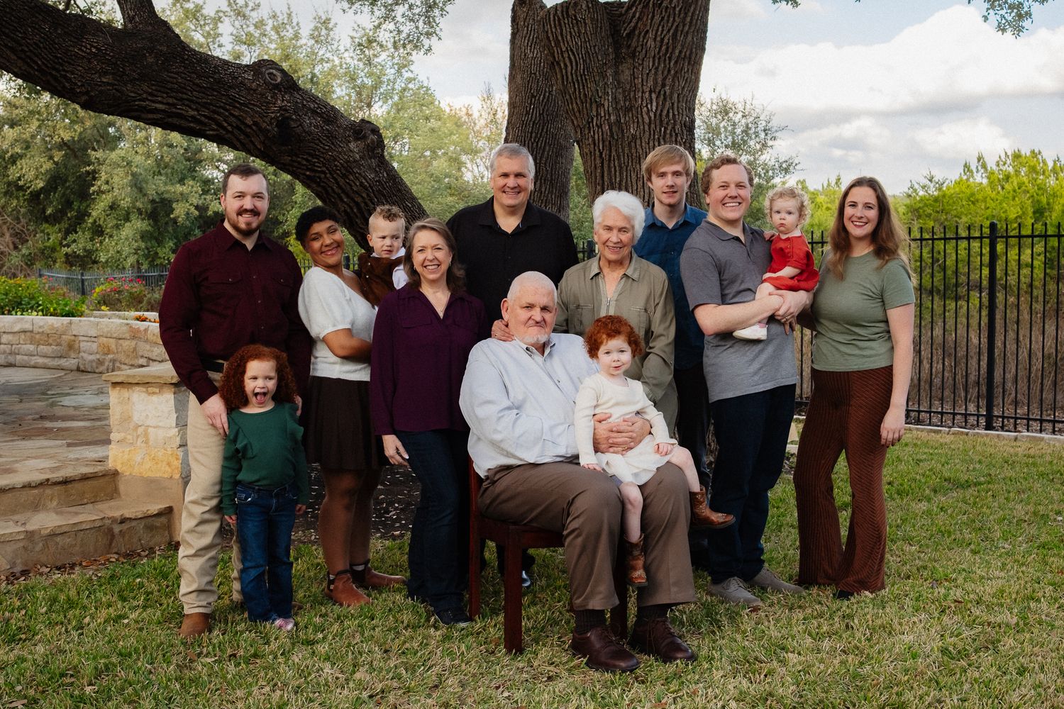 Extended family gathering posed together on grass under large tree branches.