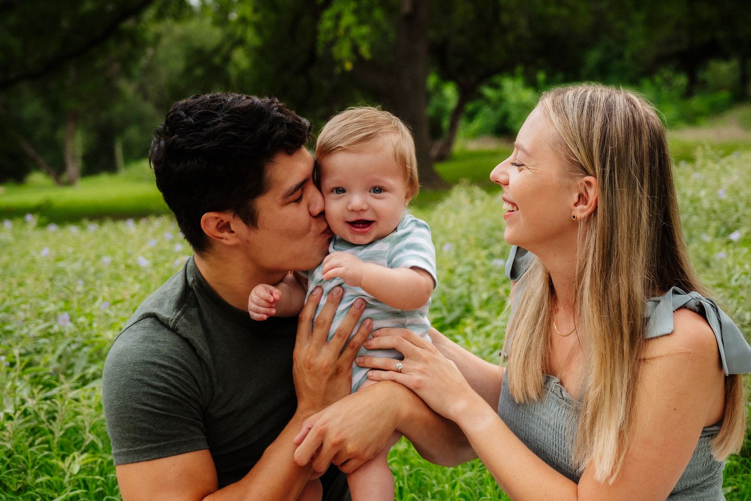 A happy family shares a joyful moment together while sitting in a grassy meadow on a sunny day.
