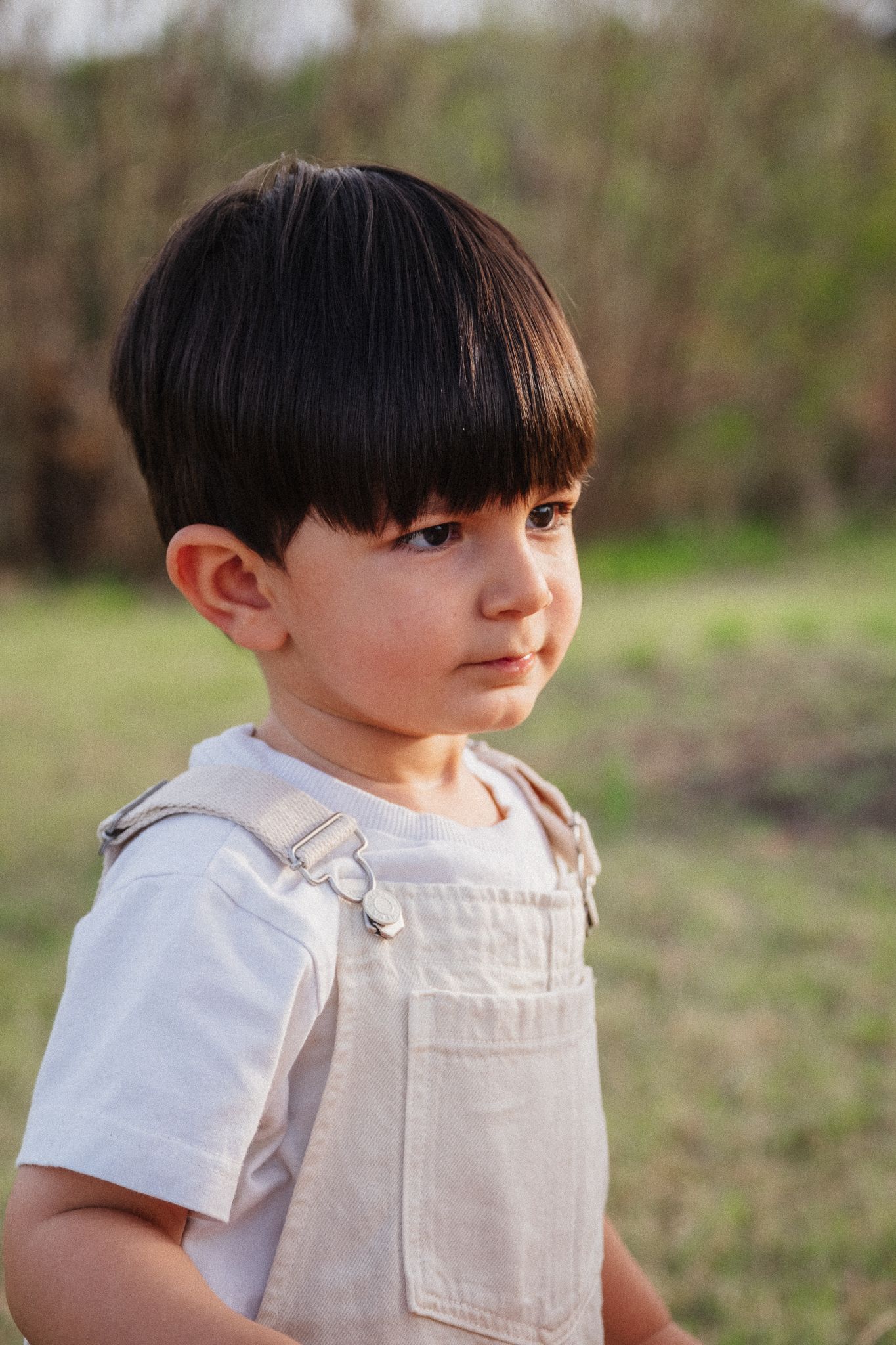 A child in a white linen outfit poses outdoors during a series of candid shots in a natural setting.