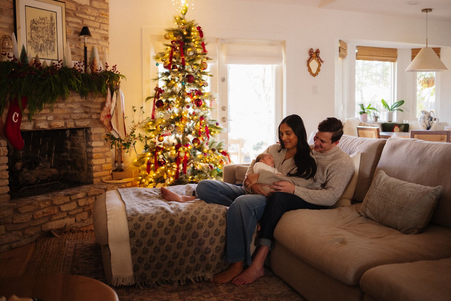Couple sitting on couch by decorated Christmas tree and fireplace in cozy living room during holiday season.