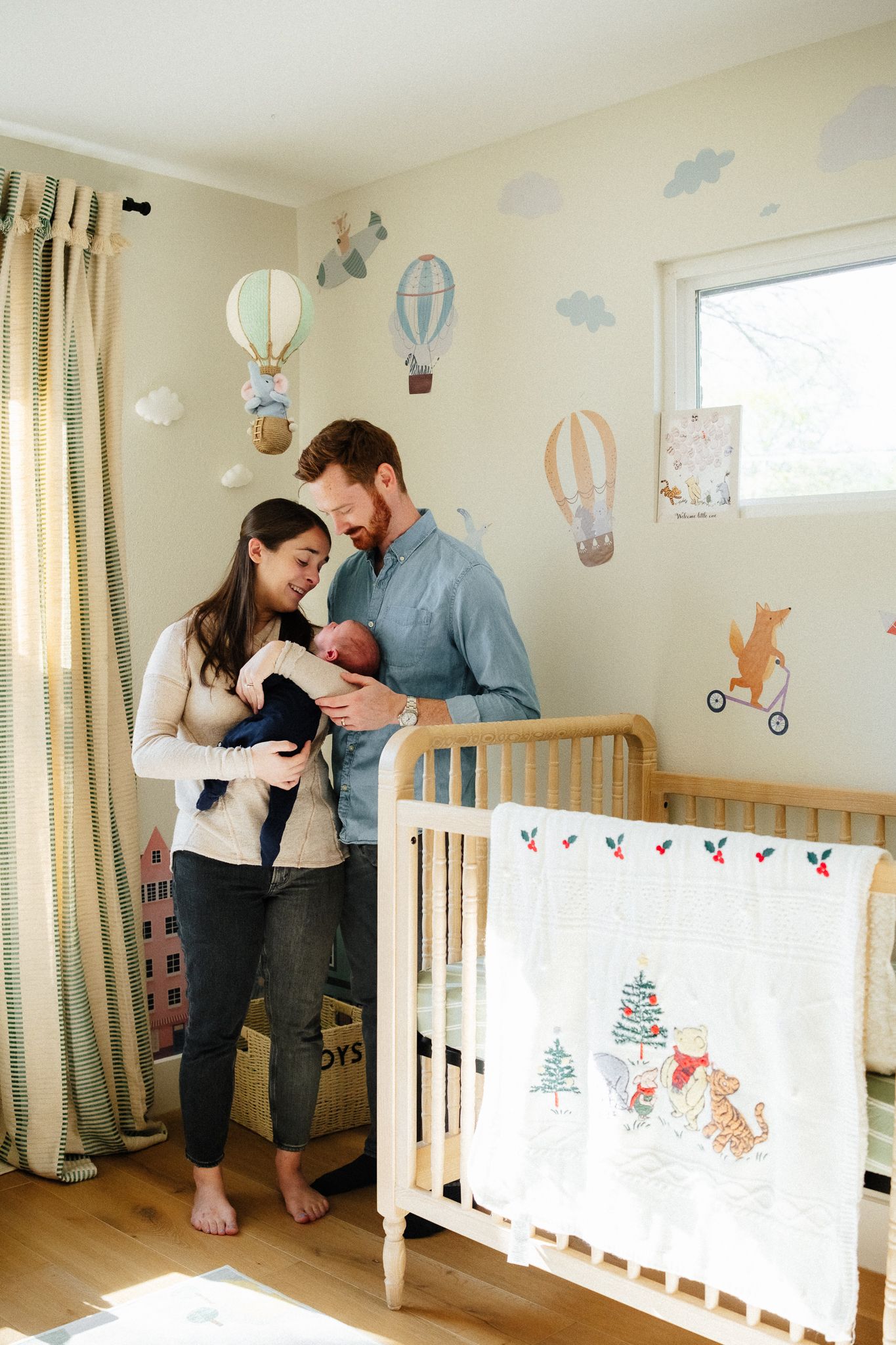 A heartwarming nursery scene with parents cradling their newborn beside a wooden crib with decorative wall decals.