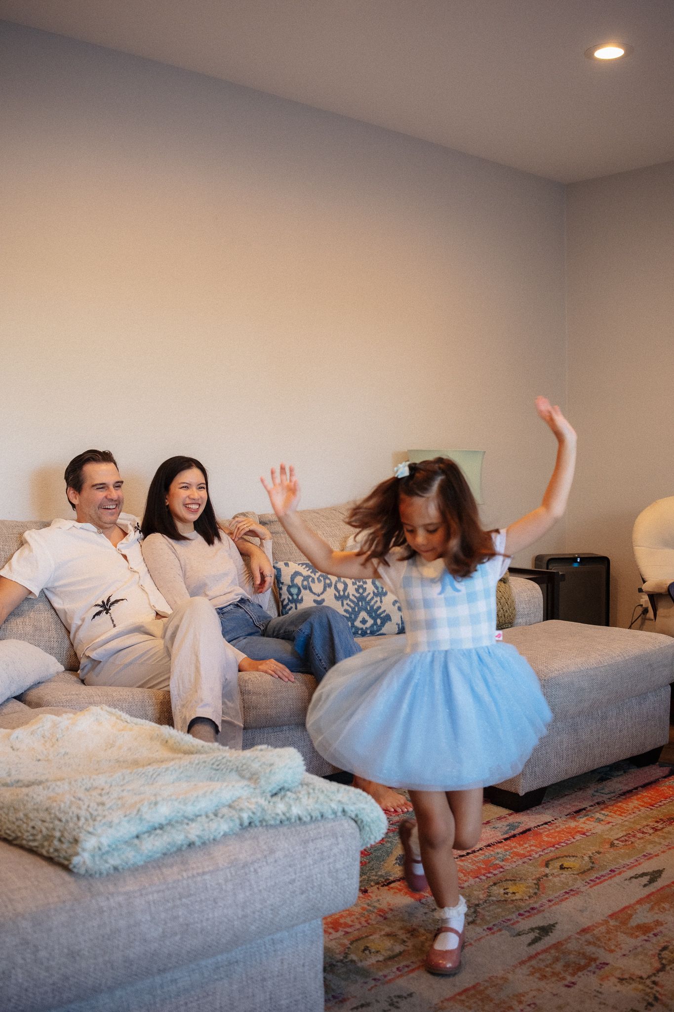 Family having fun jumping and playing together on a gray couch in a living room.