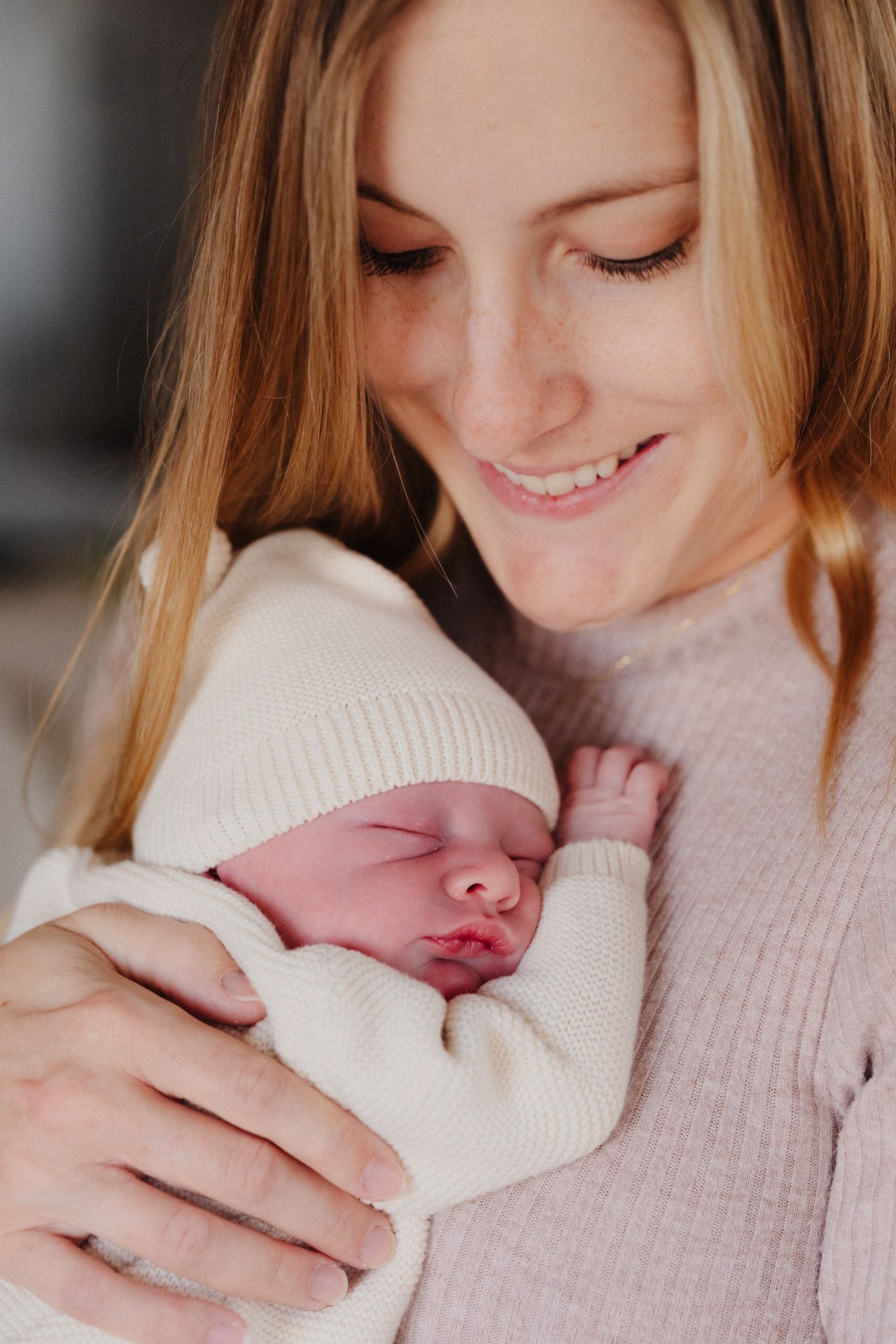 A mother in a soft pink sweater holds her sleeping newborn baby in a series of tender moments.