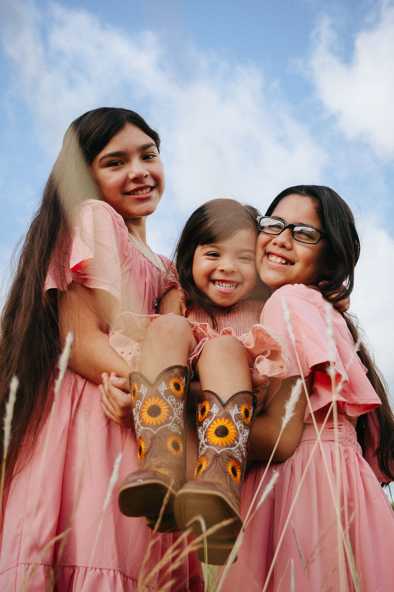 A group wearing matching pink dresses poses together while holding paper owl decorations on sticks.