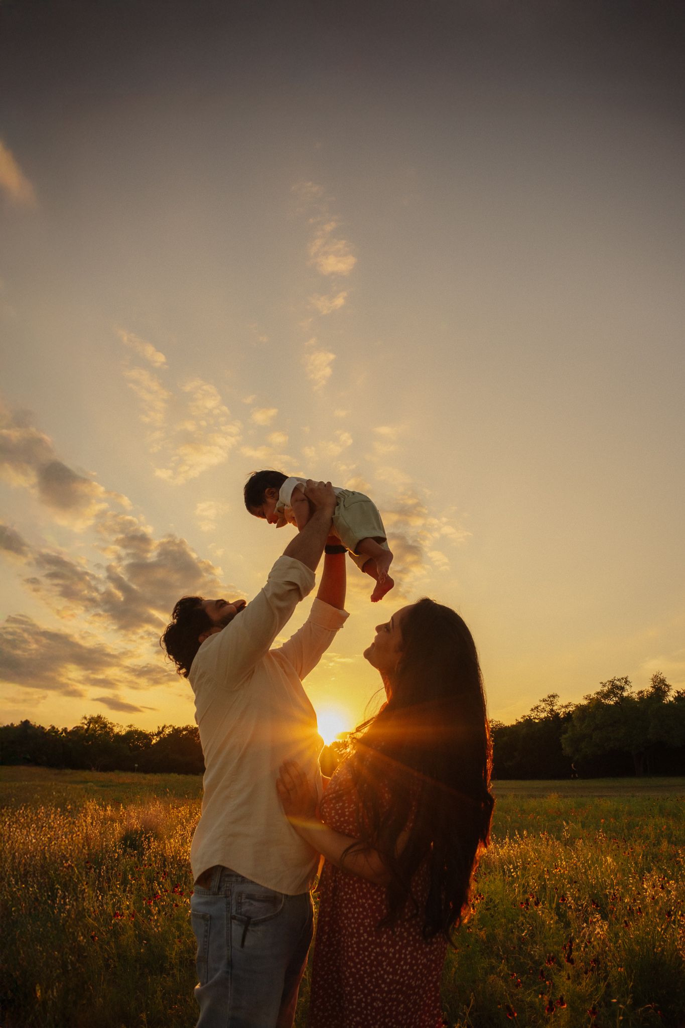 A family enjoys a tender sunset moment in a golden field as rays of sunlight illuminate their silhouettes.