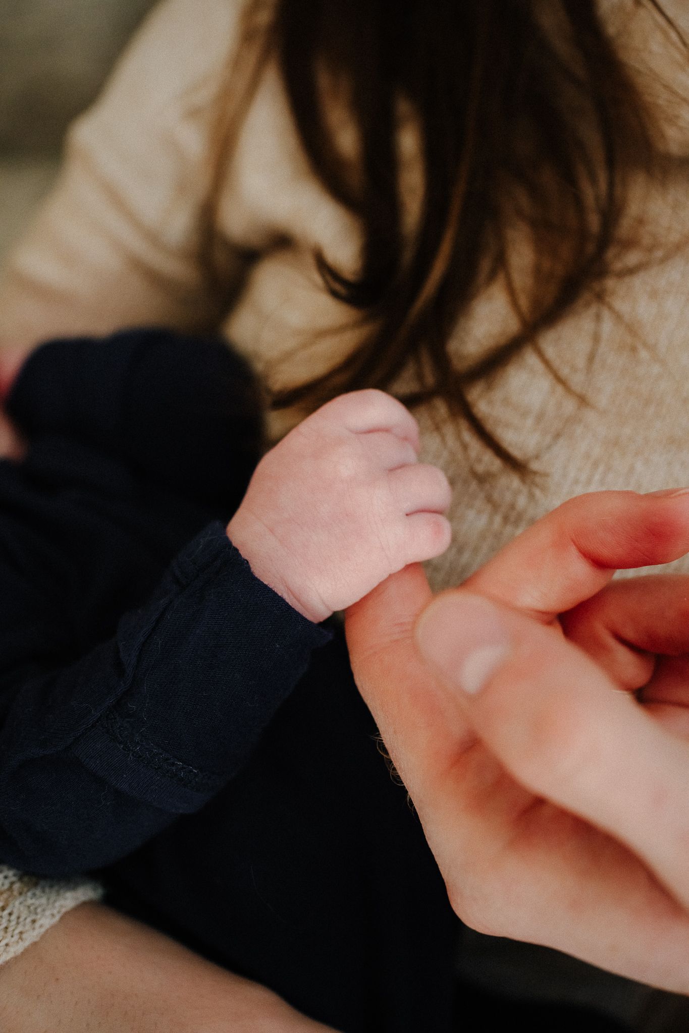 A close-up shot shows tiny baby fingers being held by adult hands against a soft fabric background.