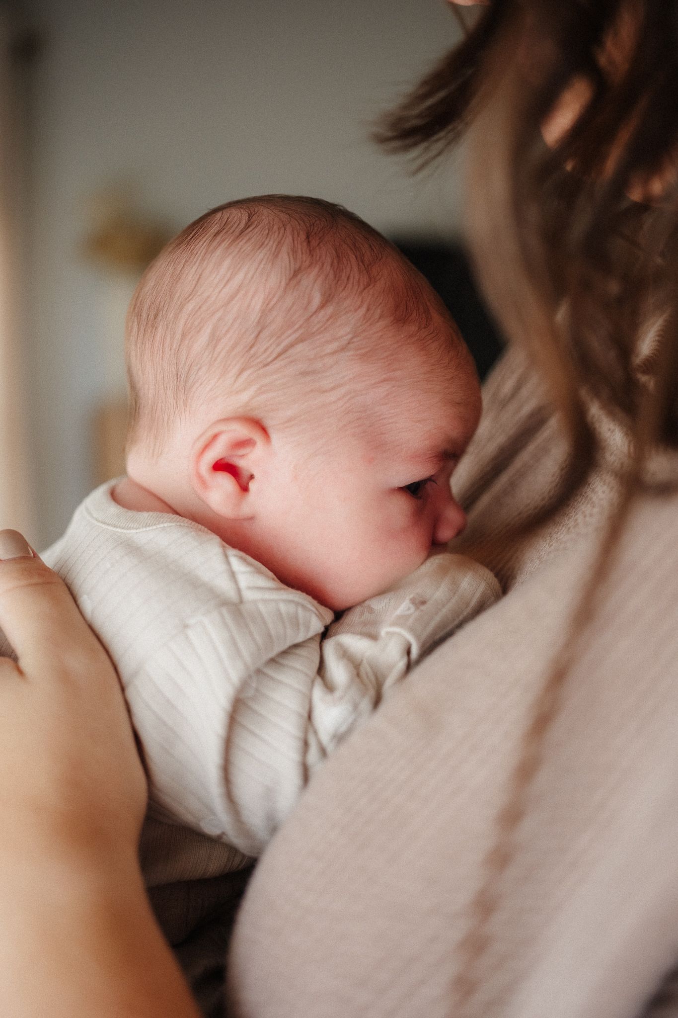 Close-up view of a sleeping newborn nestled against someone wearing a beige sweater.