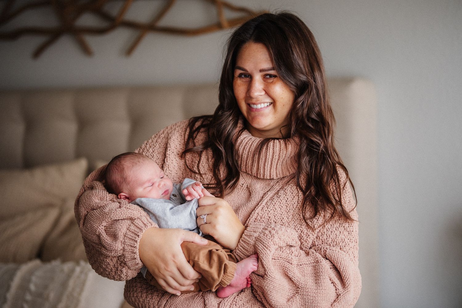 Cozy lifestyle photos showing a woman in pink sweater with a newborn in natural light.