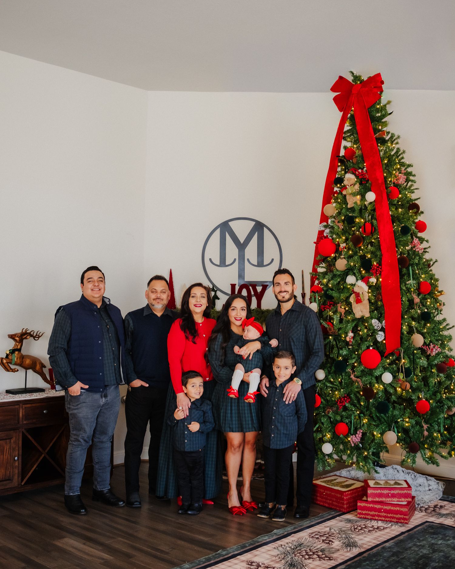 Family gathering around a beautifully decorated Christmas tree with red ornaments and bows during holiday celebrations.