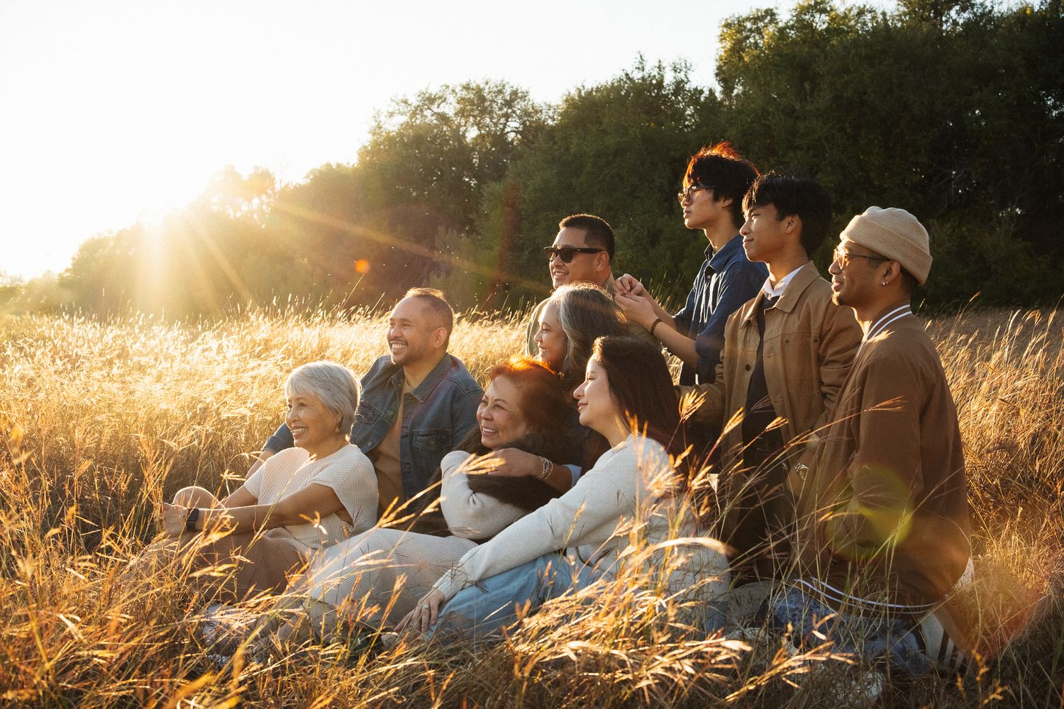 Multi-generational family sitting together in golden wheat field at sunset, sharing joyful moments outdoors.