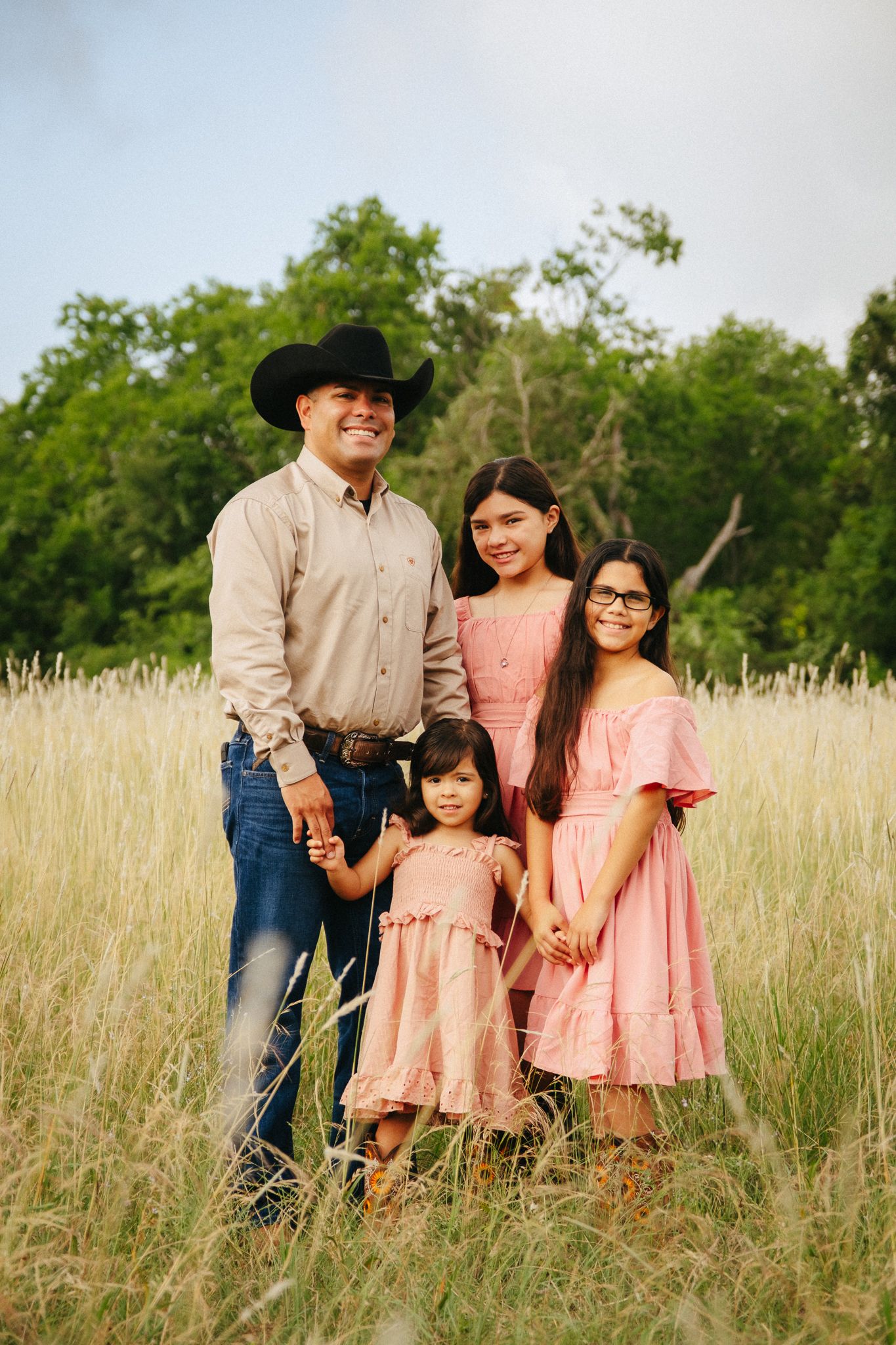 A family stands together in a sunlit field of tall grass on a summer evening.
