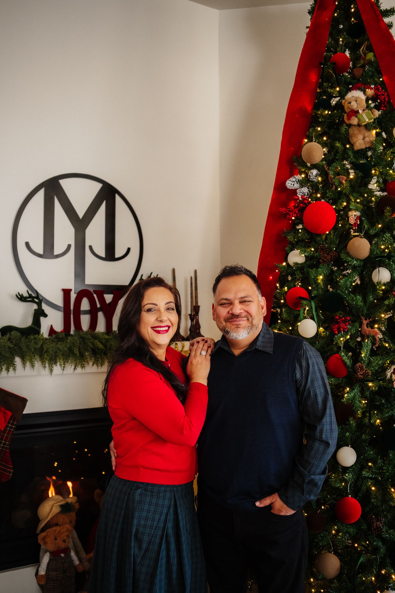 An elegant holiday setting featuring a Christmas tree with red decorations and a 'JOY' wall sign.