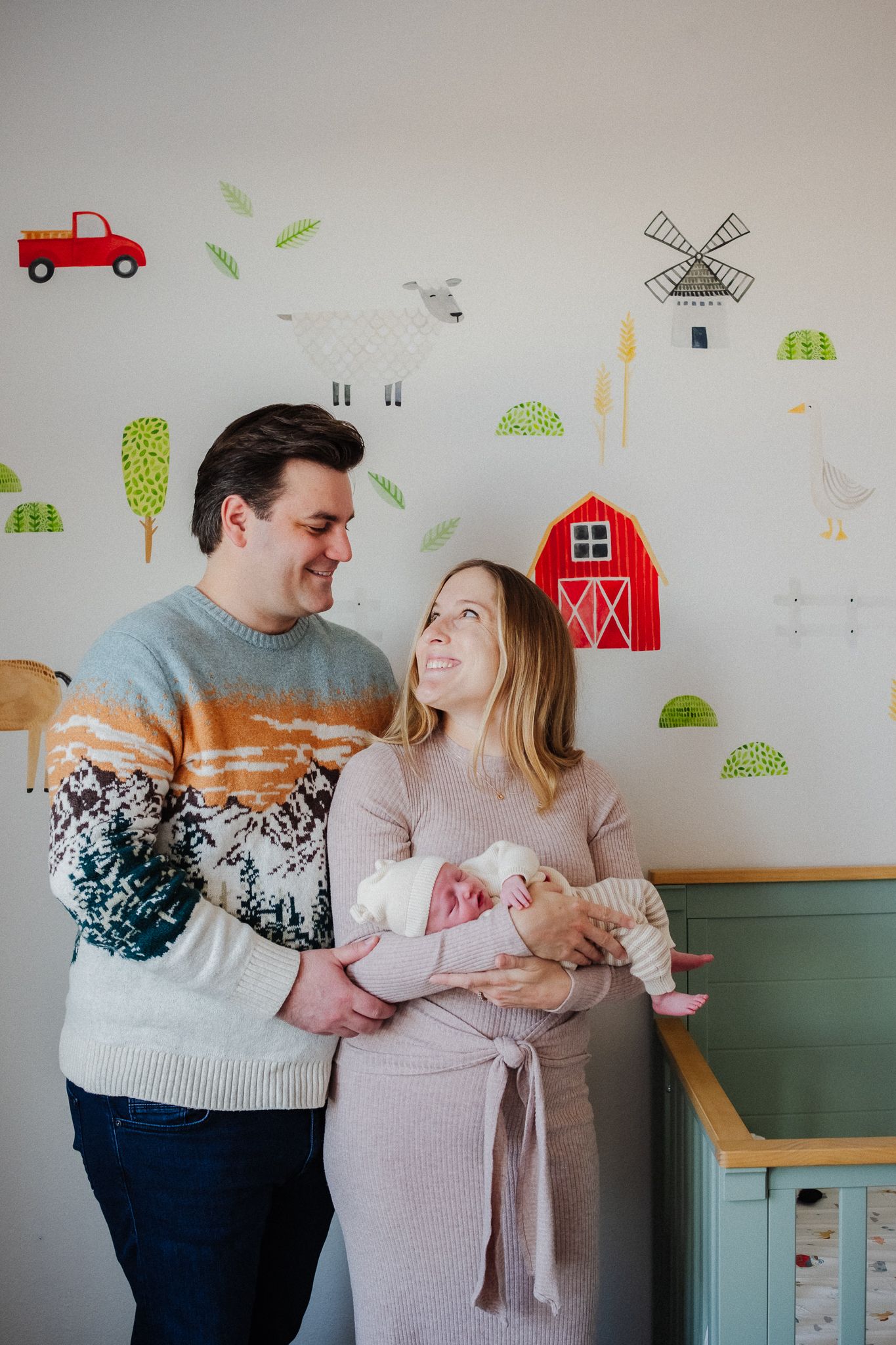 A couple stands together in a nursery decorated with farm-themed wall decals and a red barn illustration.