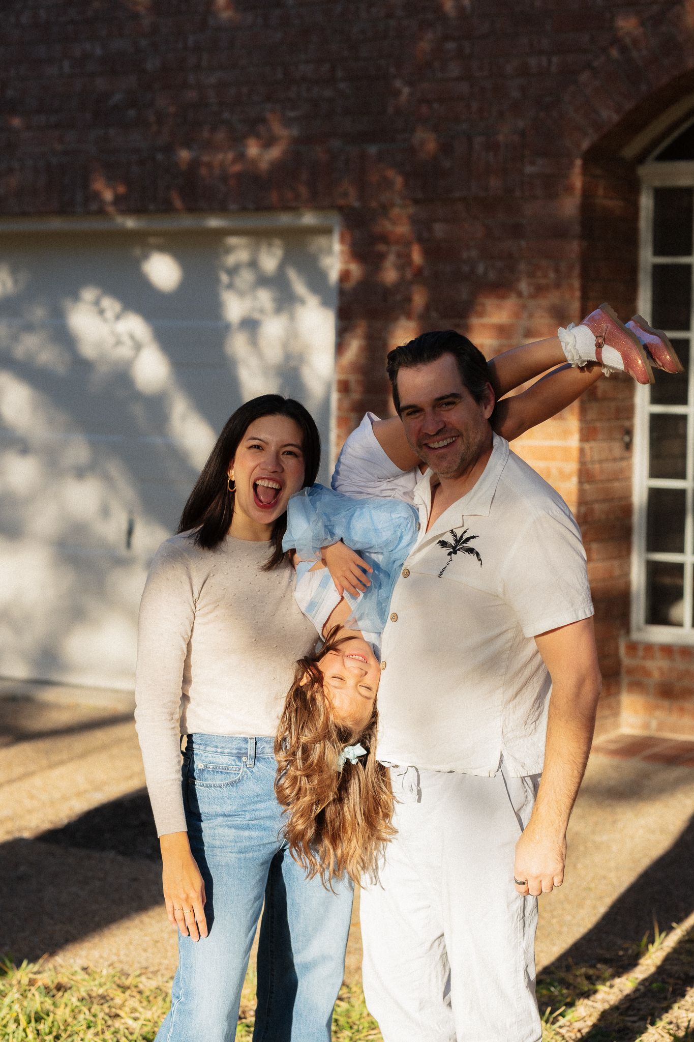 Candid outdoor family photoshoot showing playful moments against a brick wall backdrop in natural lighting.