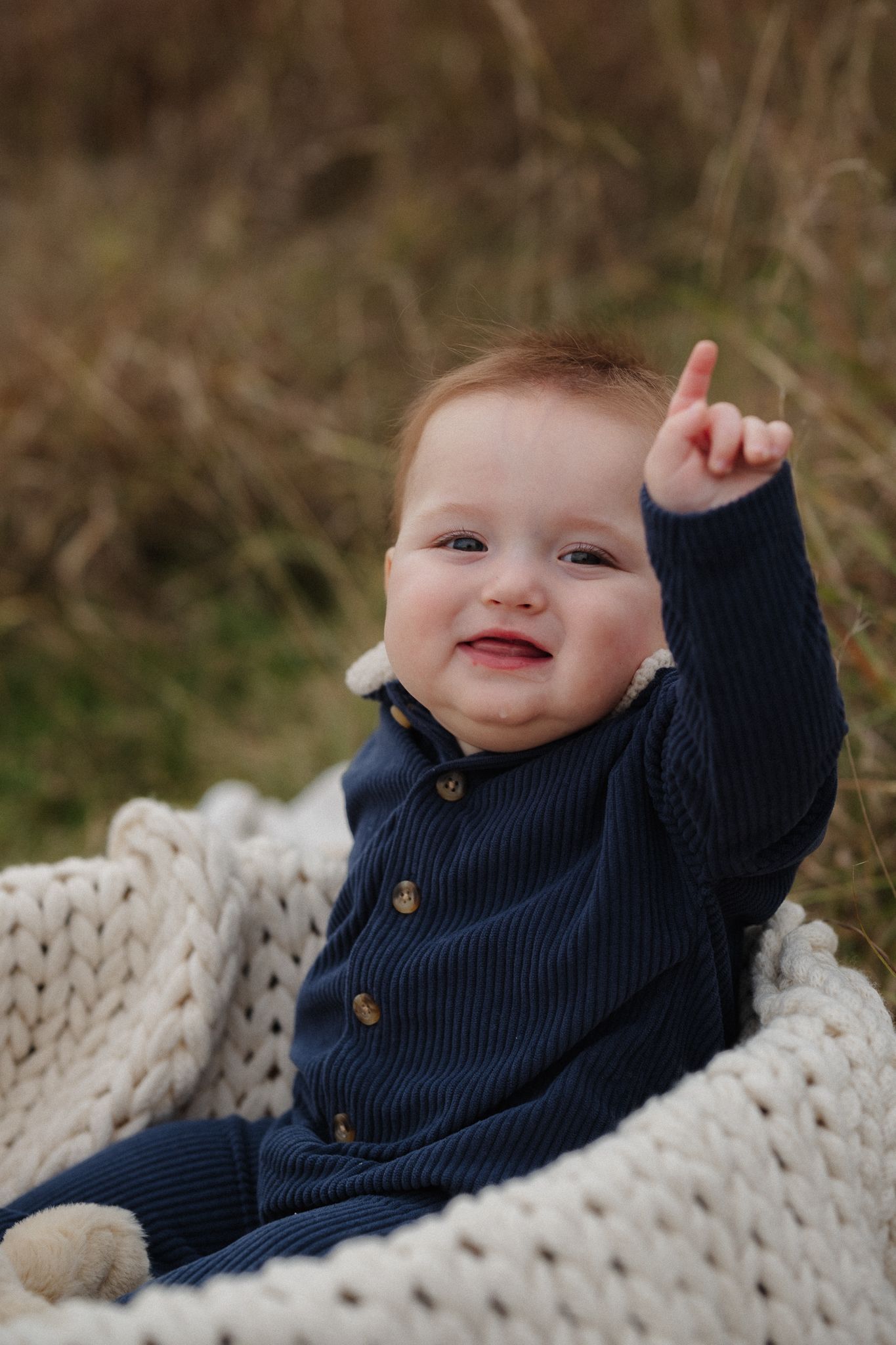 Baby in navy blue sweater lies on cream knit blanket showing playful expressions in sequence of photos.