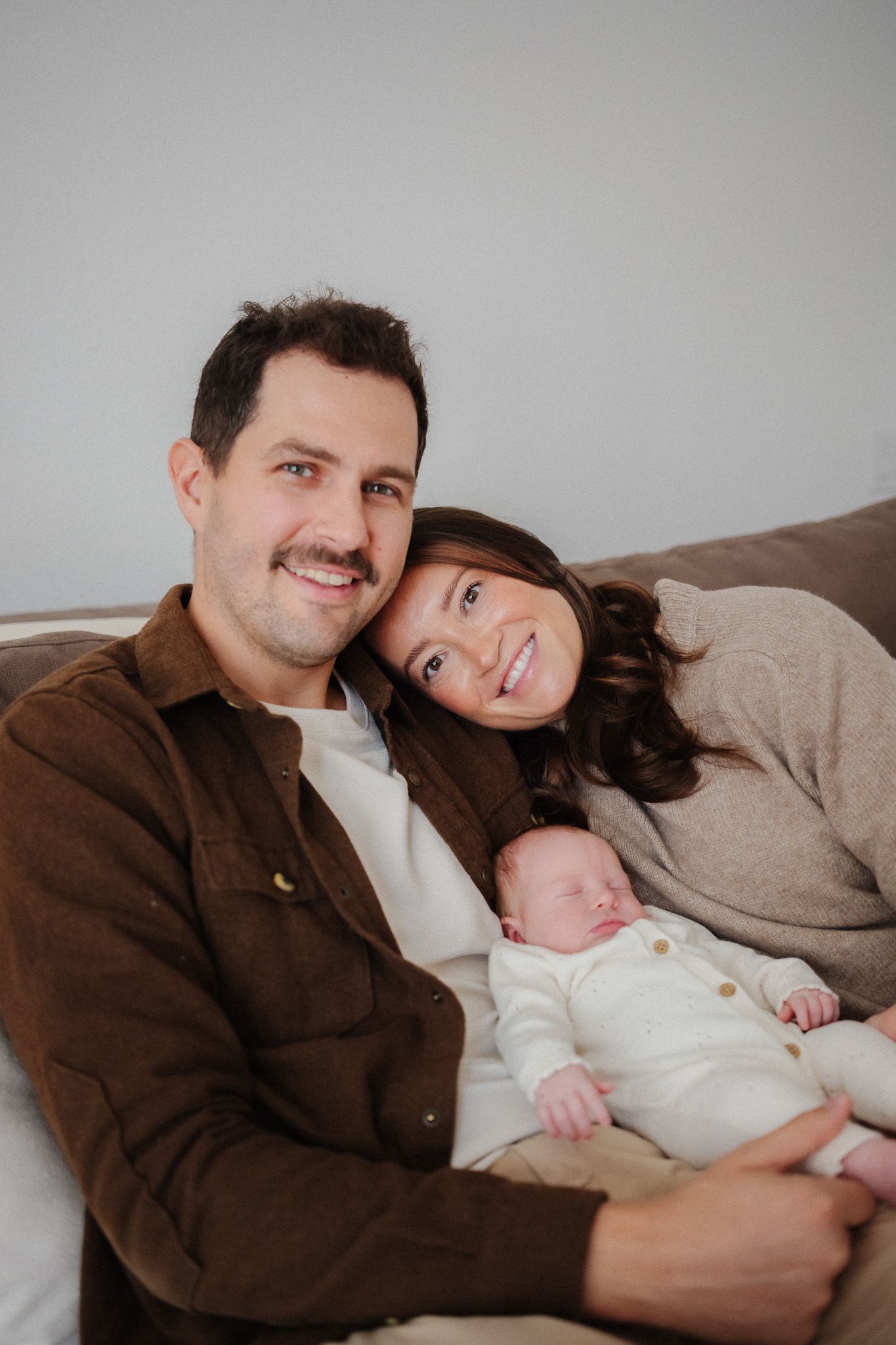 An intimate family portrait showing parents resting with their newborn on a cozy couch.