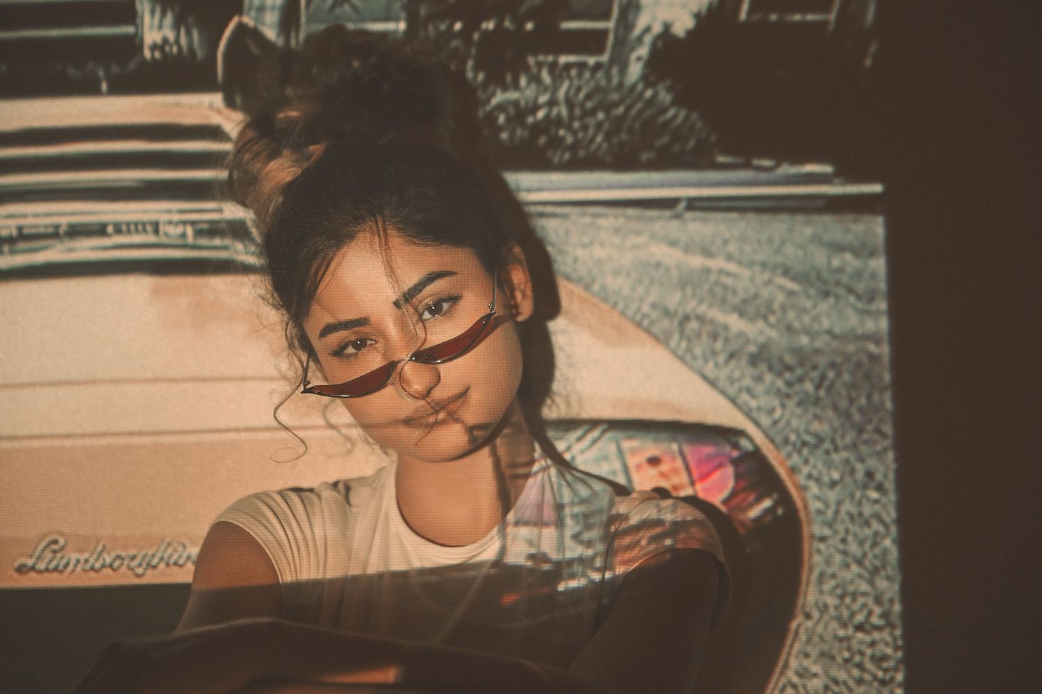 Vintage-style photo showing someone wearing glasses and a messy bun hairstyle sitting in a car interior.