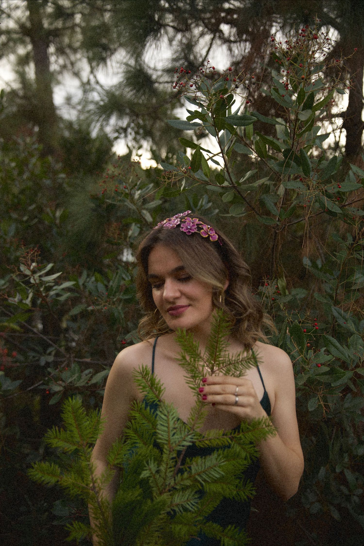 A dreamy forest scene shows someone in a floral crown amongst ferns and greenery at dusk.