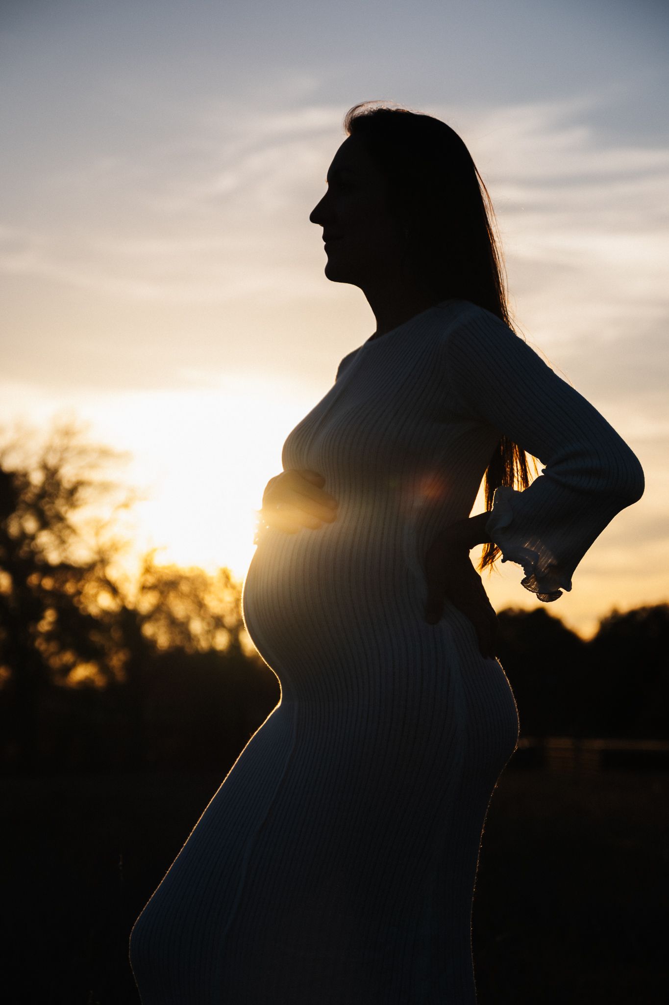 Silhouette of pregnant woman in a dress standing against vibrant sunset sky during golden hour maternity photoshoot.