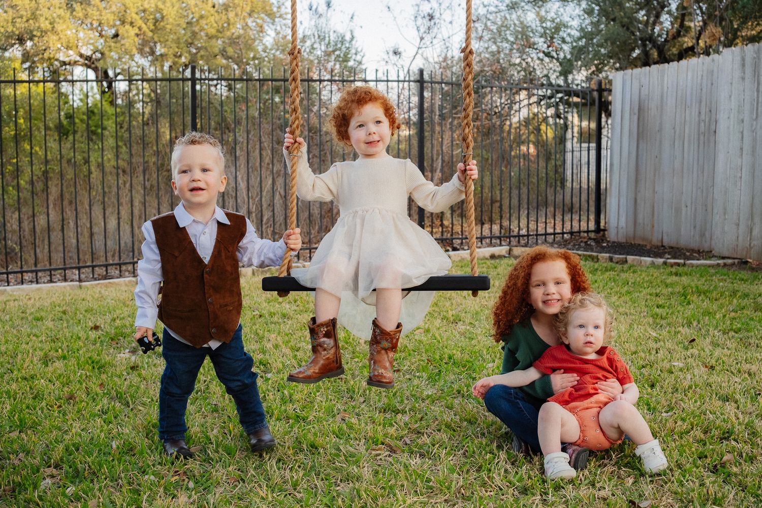 Children playing and running through a grassy yard with a fence in the background.