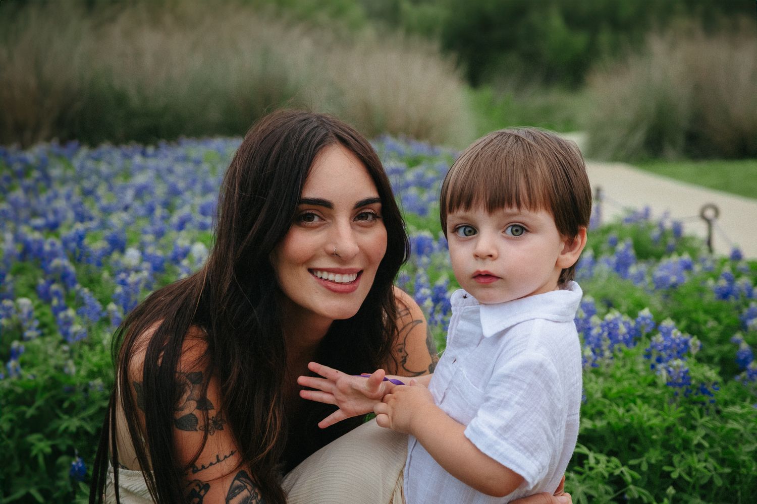 A parent and young child pose together in a field of blooming bluebonnets on a spring day.