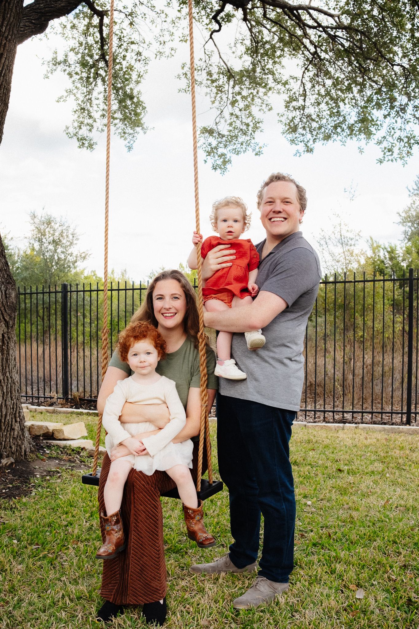 A family shares a joyful moment together by a rope swing under a shady tree in their backyard.