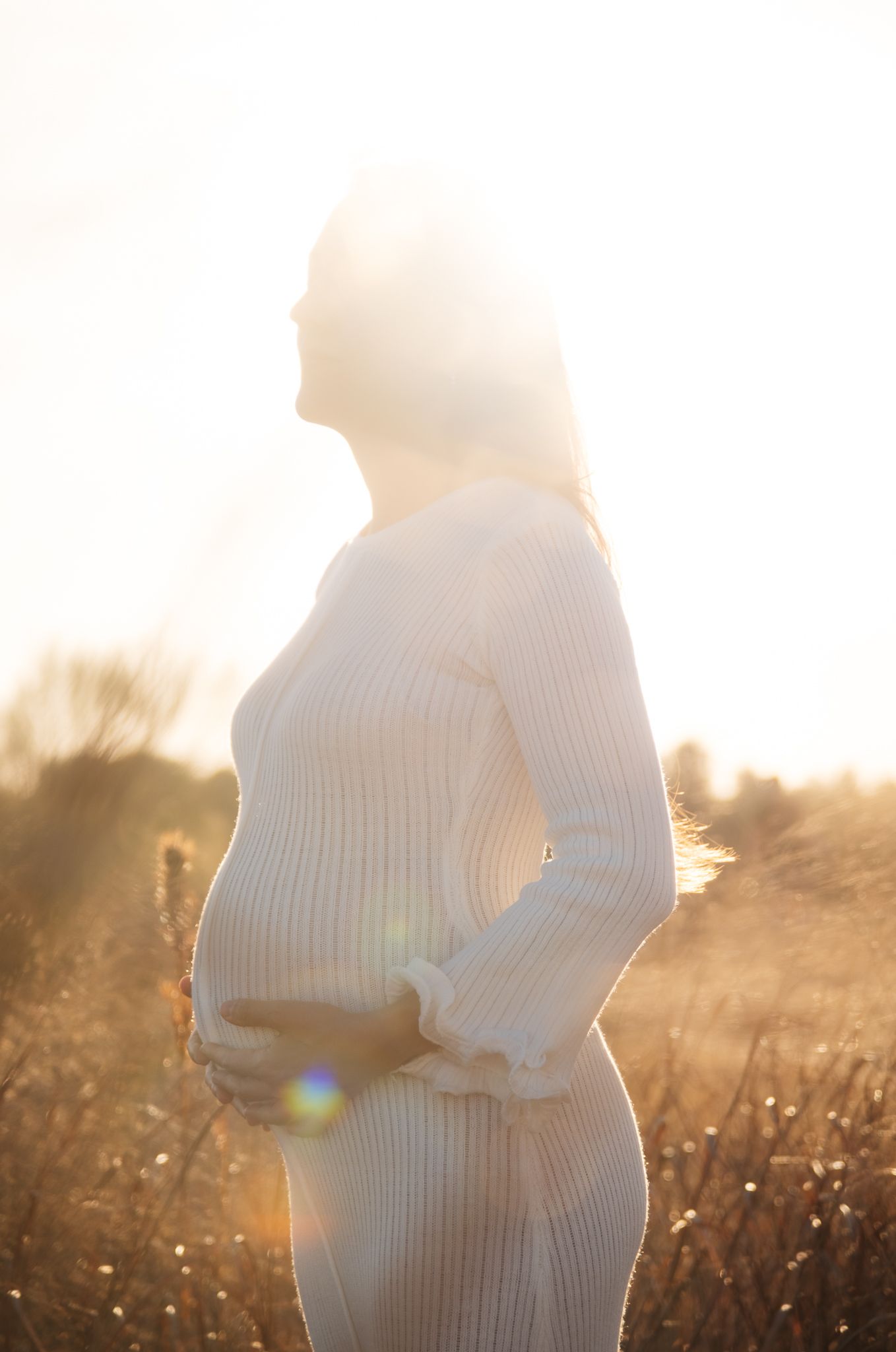 A silhouetted figure in a white sweater stands in a sunlit field during golden hour.