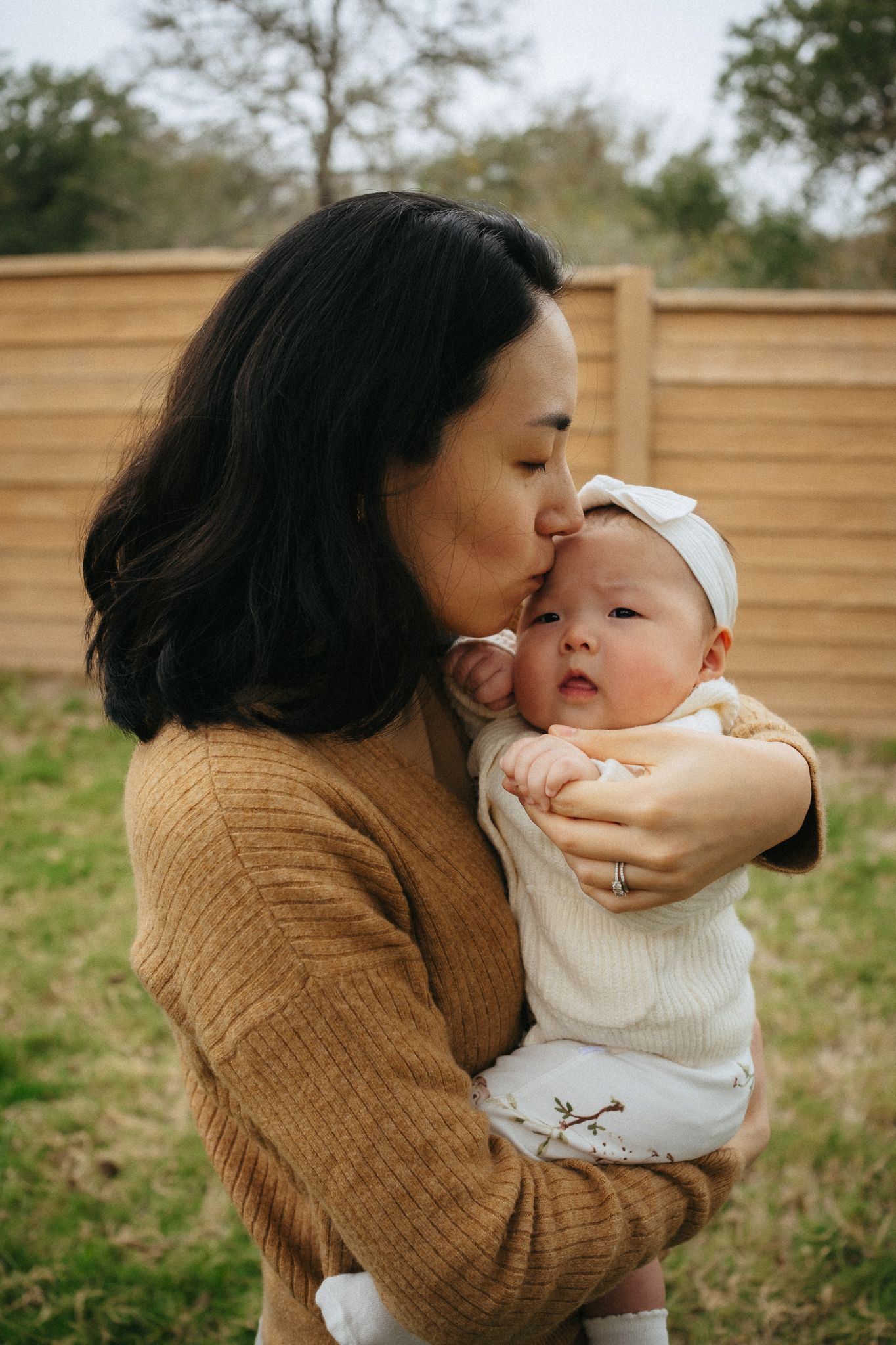 A tender moment shared between parent and baby outdoors against a wooden fence backdrop.