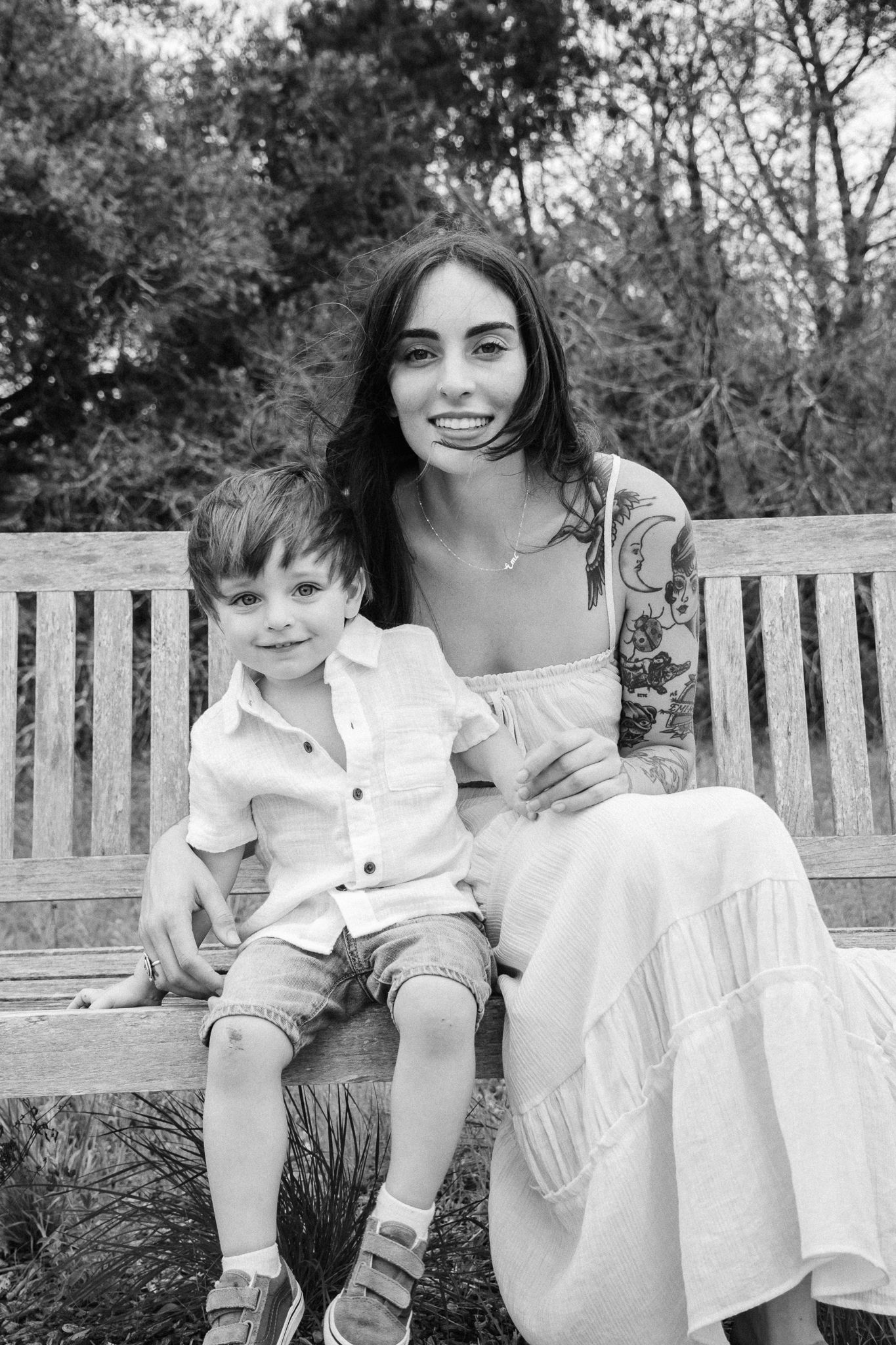 A black and white photo of an adult and young child sitting together on a wooden bench in an outdoor garden setting.