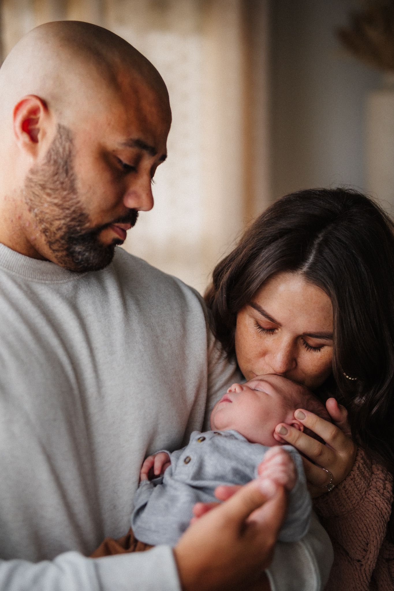 Intimate family photos showing parents sharing loving moments with their newborn in soft natural light.