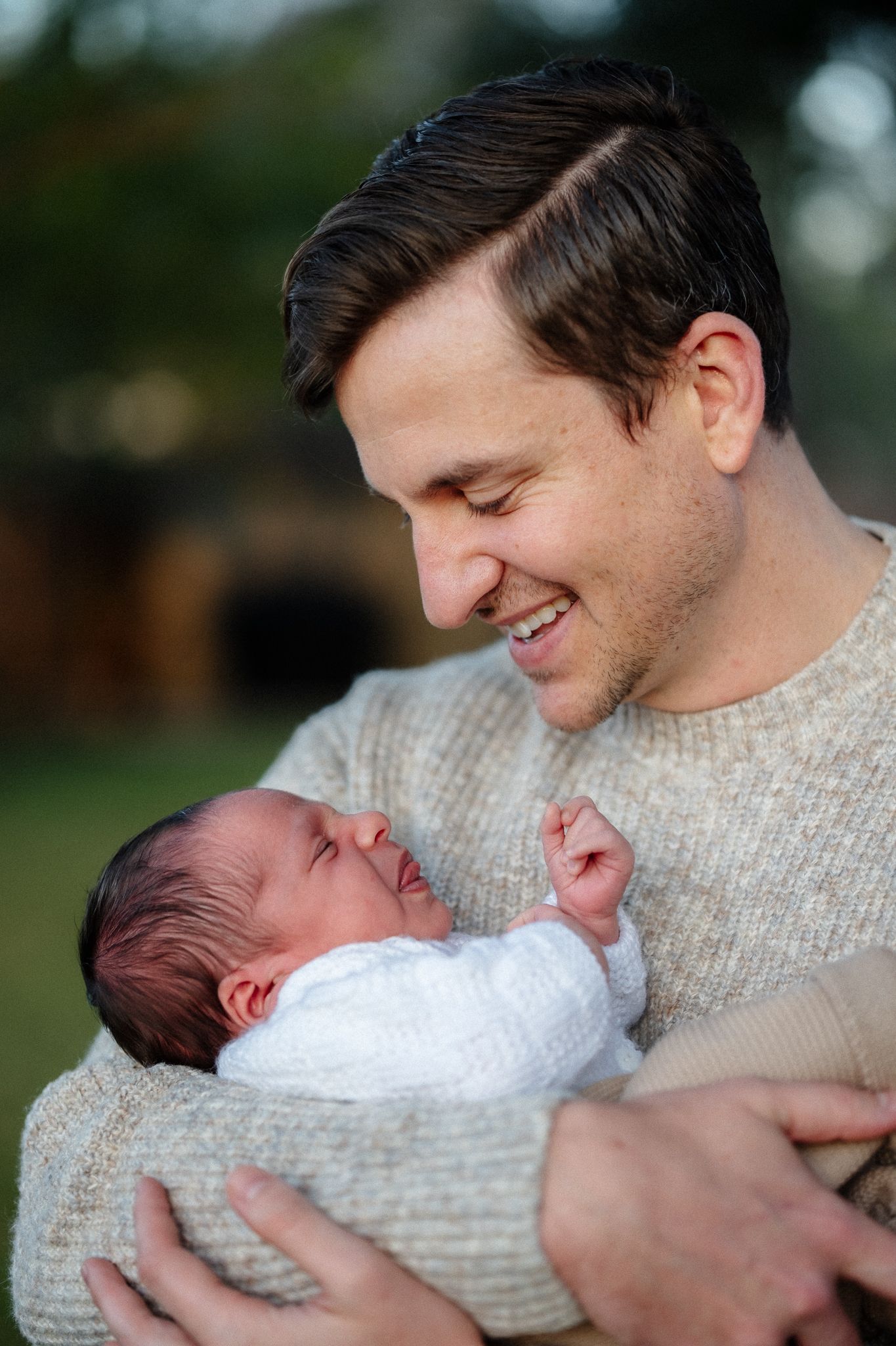 Sweet moments between parent and newborn baby captured in outdoor natural lighting.