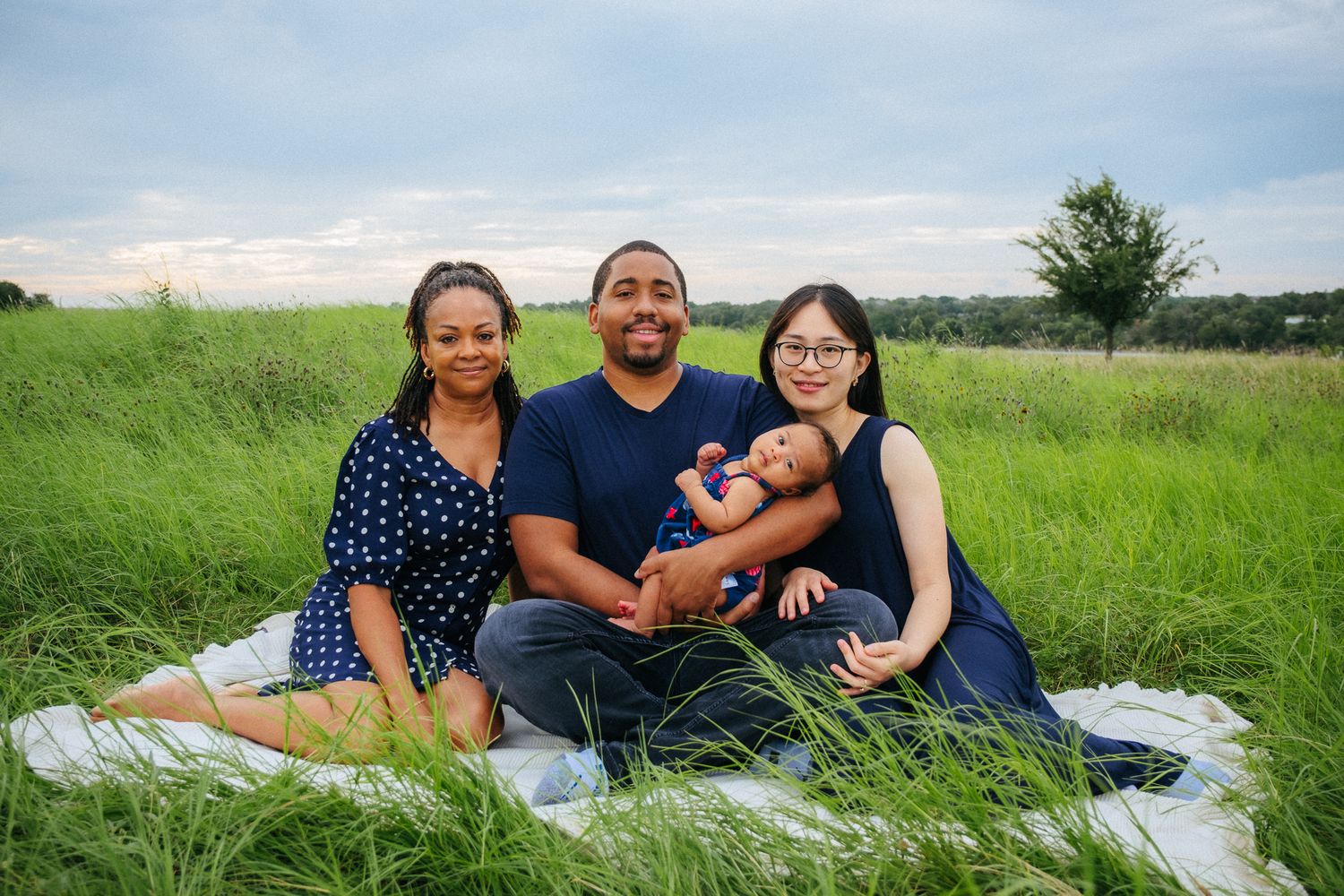 A family sits together on a blanket in a lush green meadow on a sunny summer day.