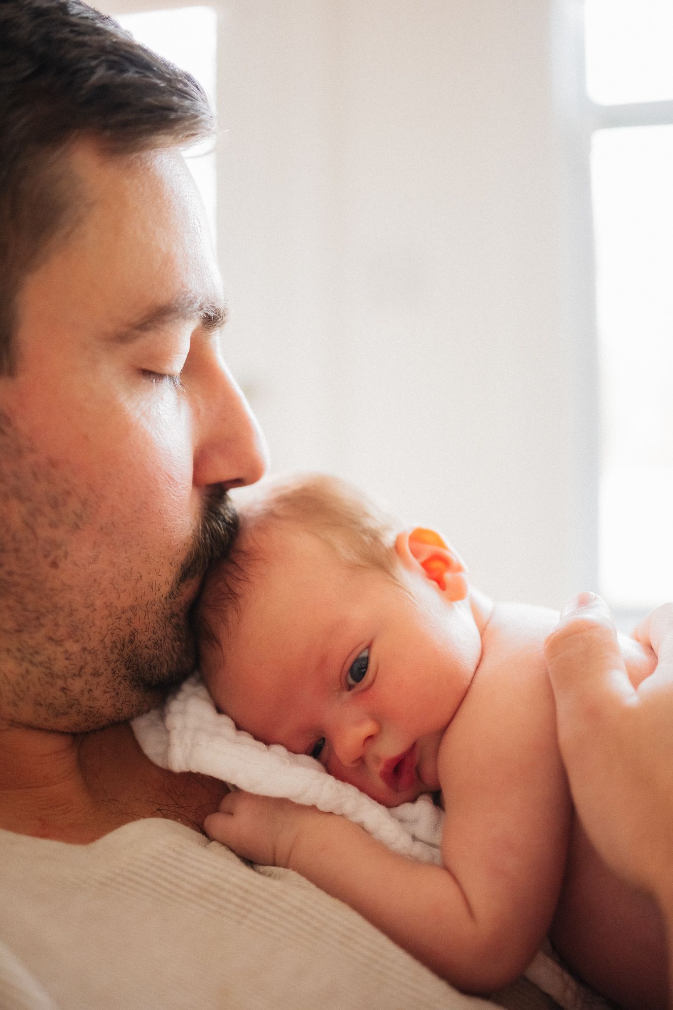A tender moment between parent and newborn baby as they share gentle kisses in soft natural light.