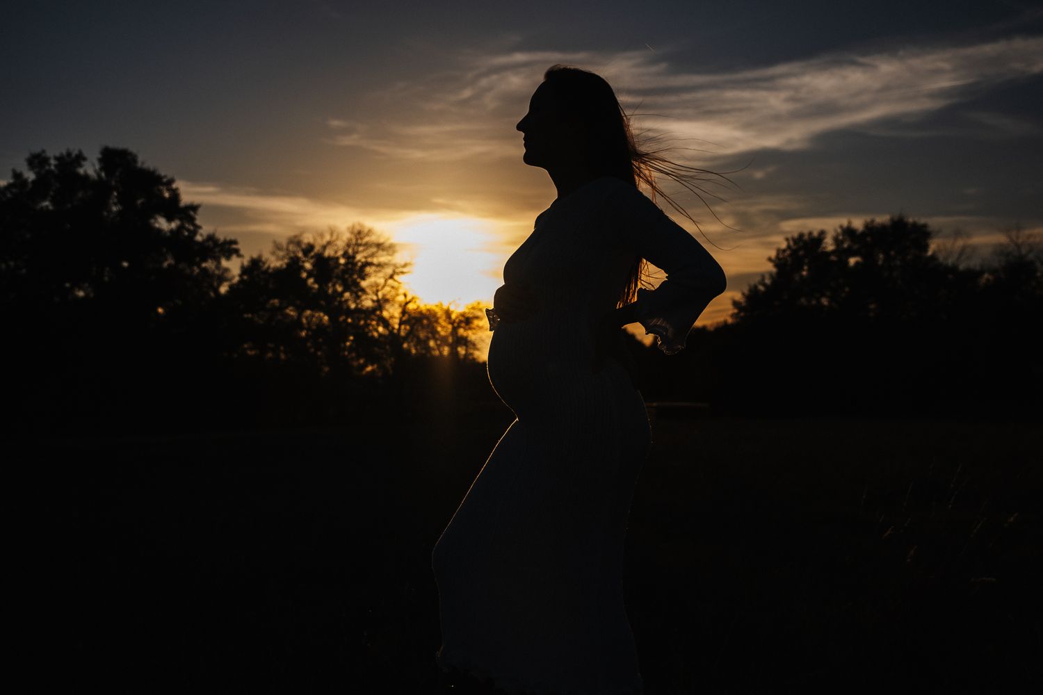 Maternity silhouette at sunset showing woman's profile against dramatic evening sky.