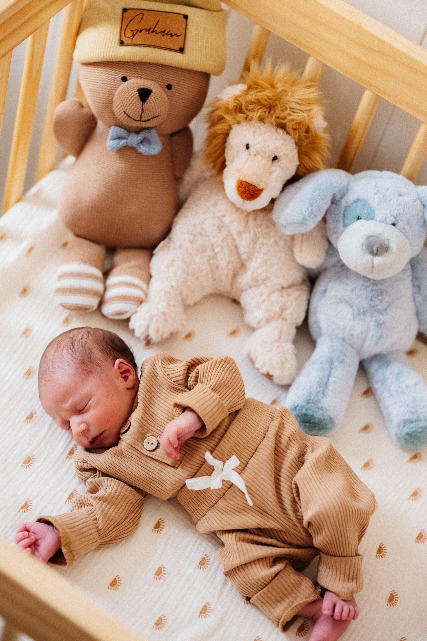 Newborn baby sleeping in a crib with stuffed animal toys including a bear, lion, and elephant.