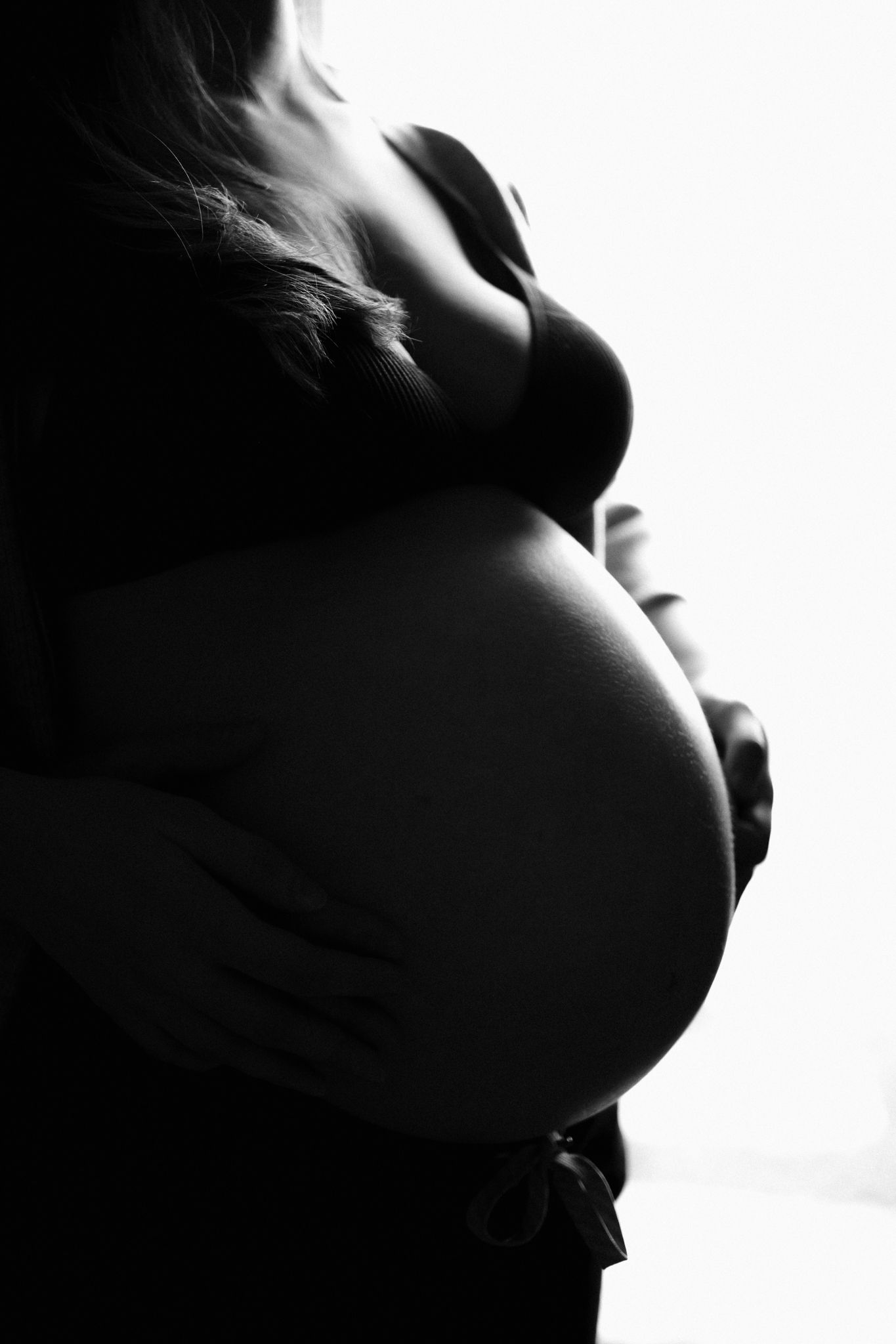 Artistic black and white silhouette highlighting a pregnant belly against white background.