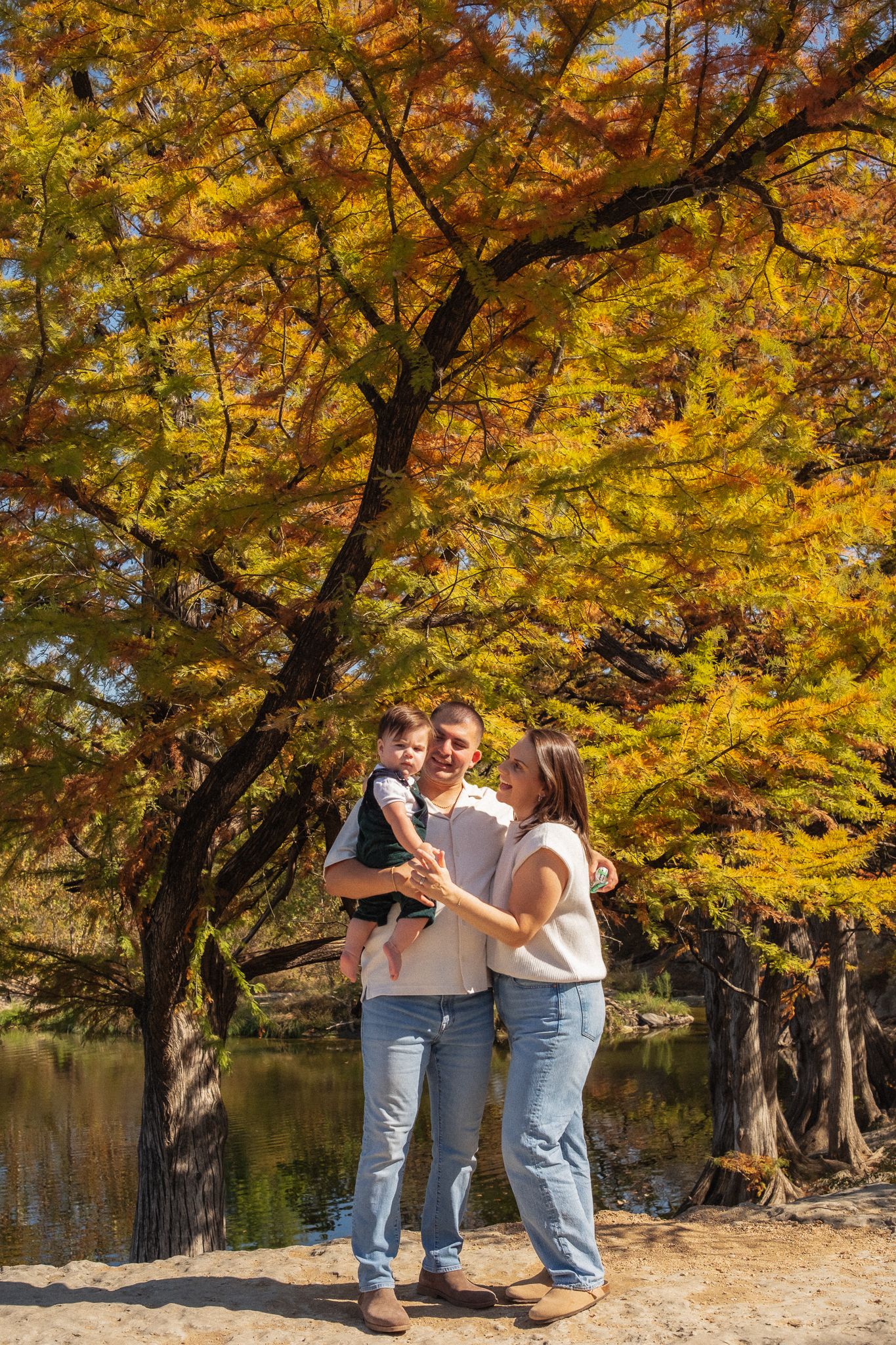 A family moment captured beneath golden autumn trees by a tranquil lake.