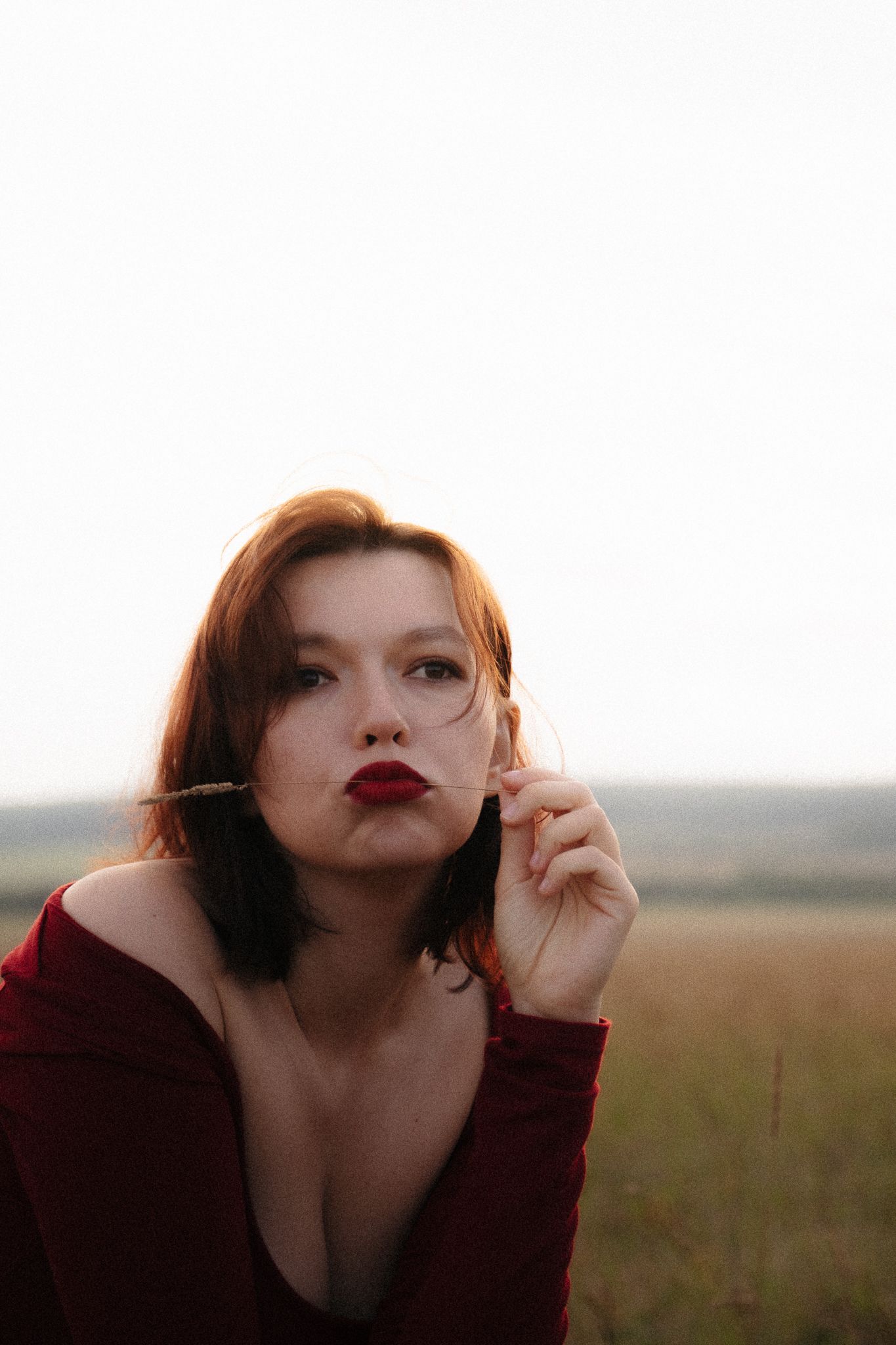 A portrait in warm tones features a person in burgundy clothing against a dreamy sunset landscape backdrop.