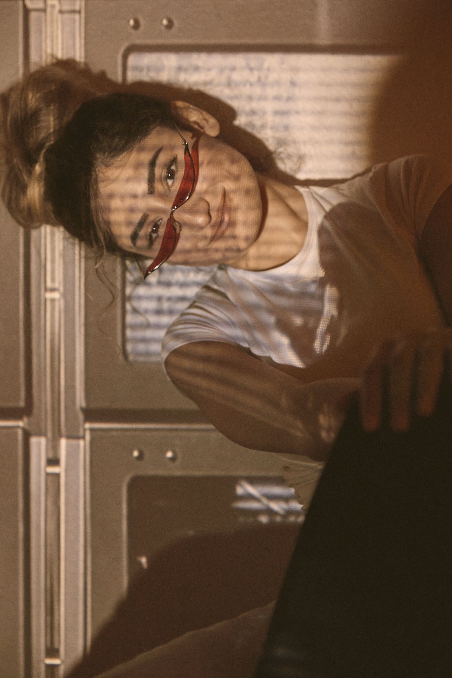A sepia-toned photo showing someone wearing red glasses and a white shirt in a softly lit indoor setting.