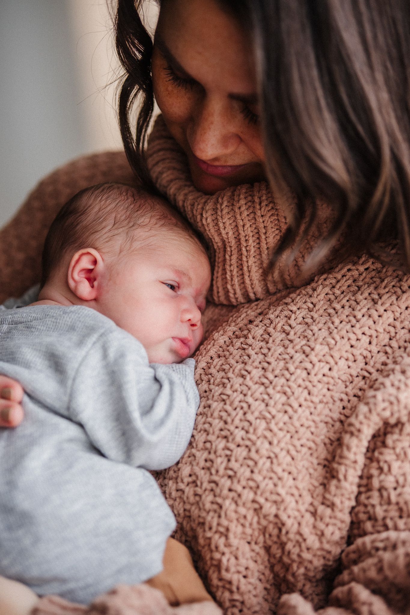 Baby in gray sleeper napping against person wearing brown knit sweater.