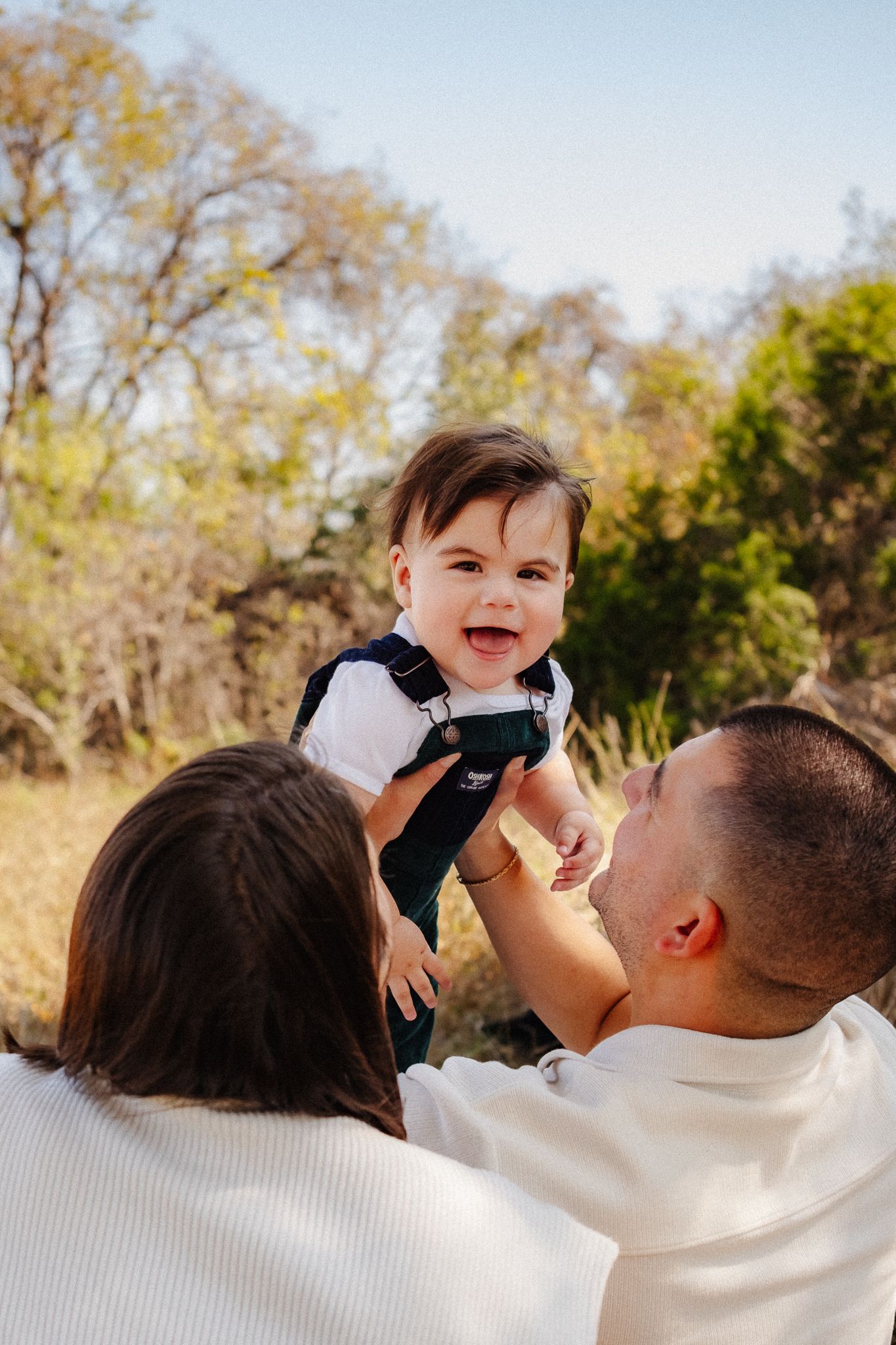 A joyful outdoor family moment captured against autumn trees and blue sky.
