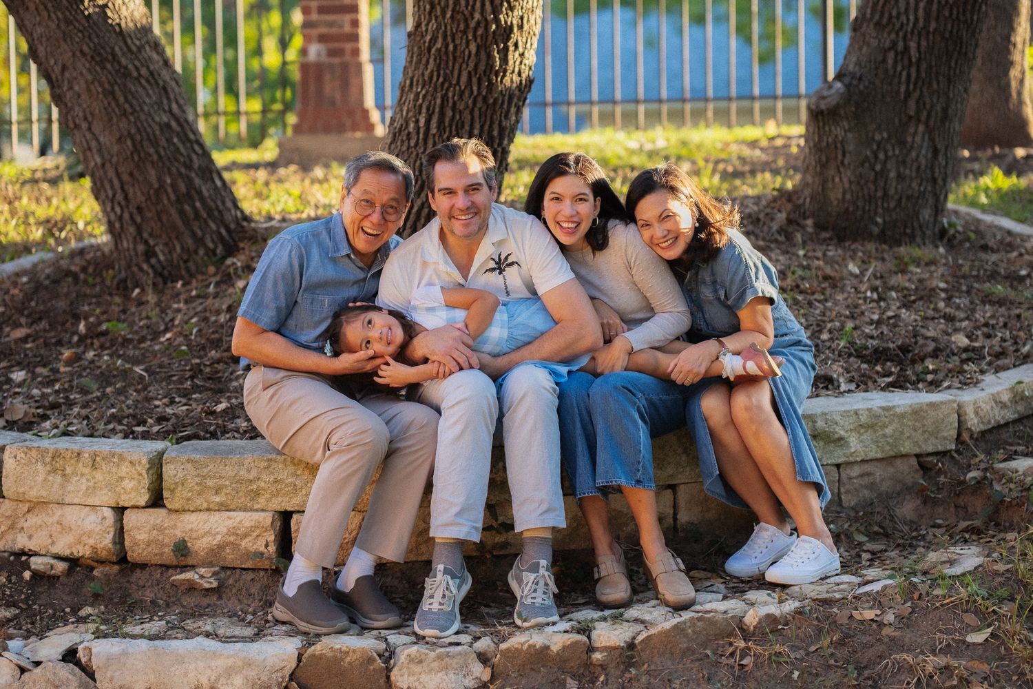 A group sits together on stone steps under trees in a park on a sunny day.