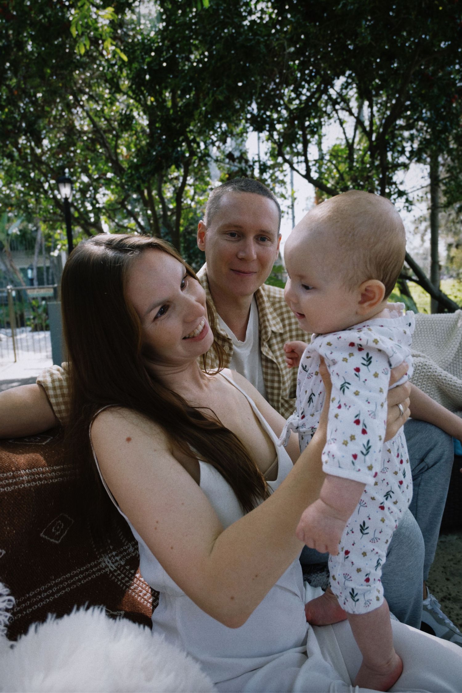 A young family spending time together outdoors on a sunny day surrounded by green trees and foliage.