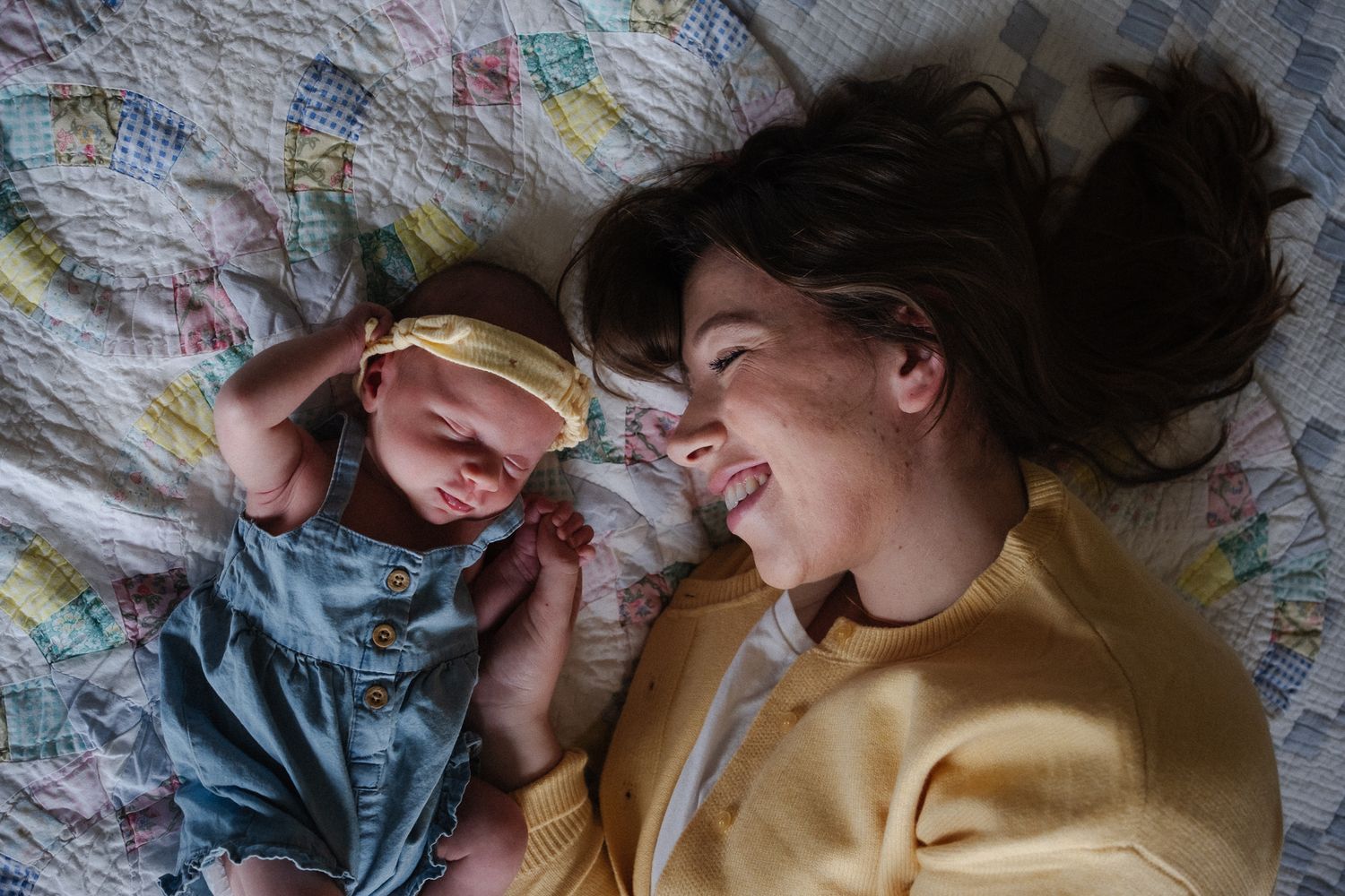 Mother and newborn baby lying on a colorful quilt bed, sharing a joyful moment together.