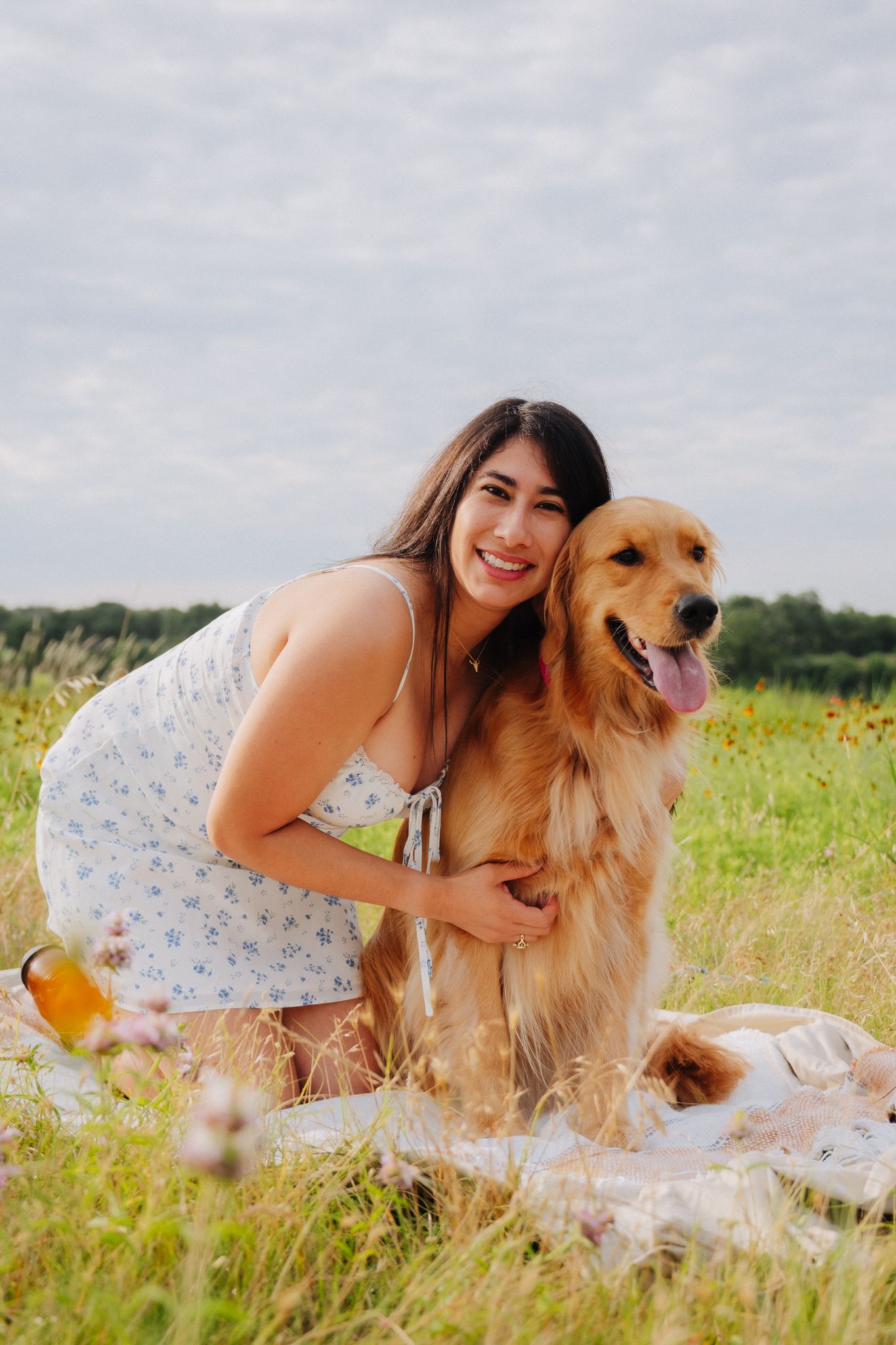 A Golden Retriever and someone enjoying a picnic together on a sunny meadow with wildflowers.