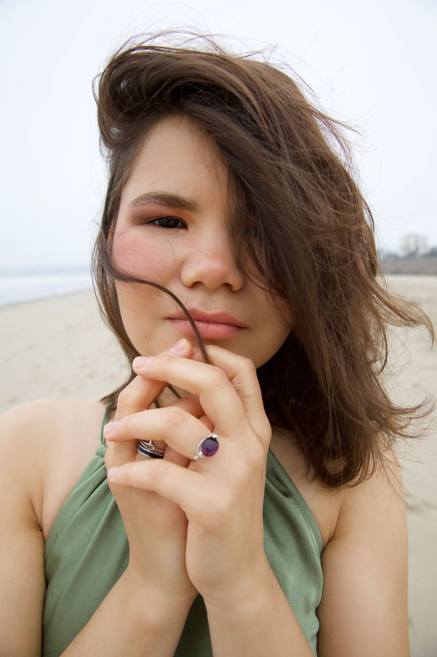 Portrait at the beach showing someone in a sage green halter top with windswept hair and a purple gemstone ring.
