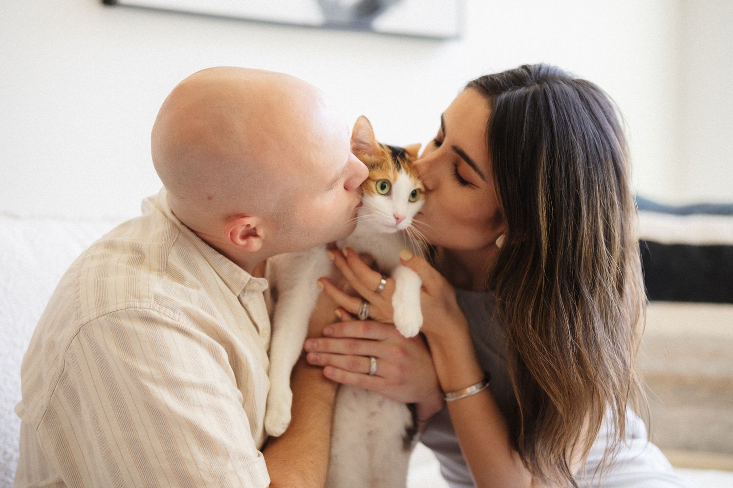 A couple shares a tender moment while holding their orange and white cat between them.