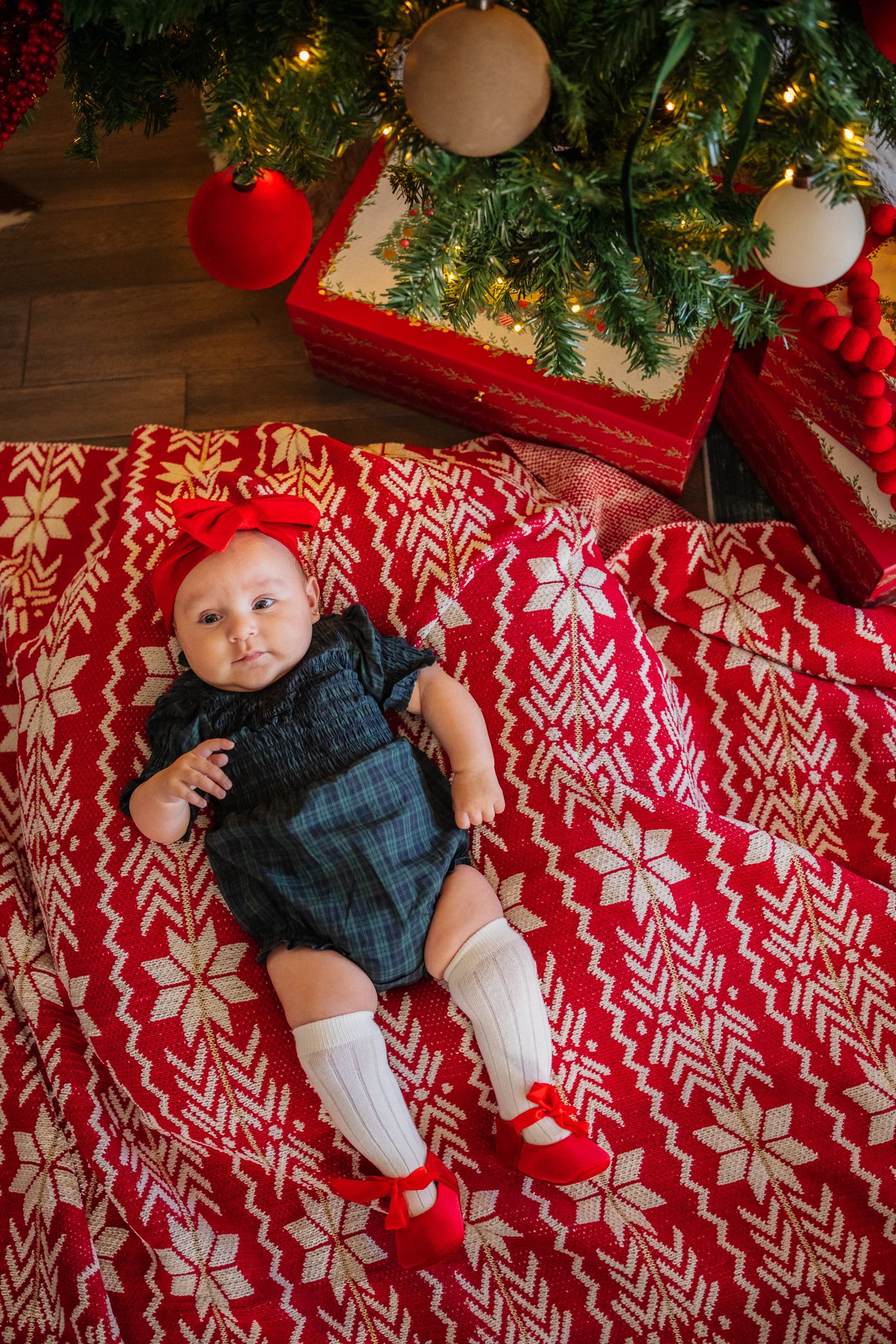 A festive holiday scene with a red and white Nordic patterned blanket under a decorated Christmas tree.