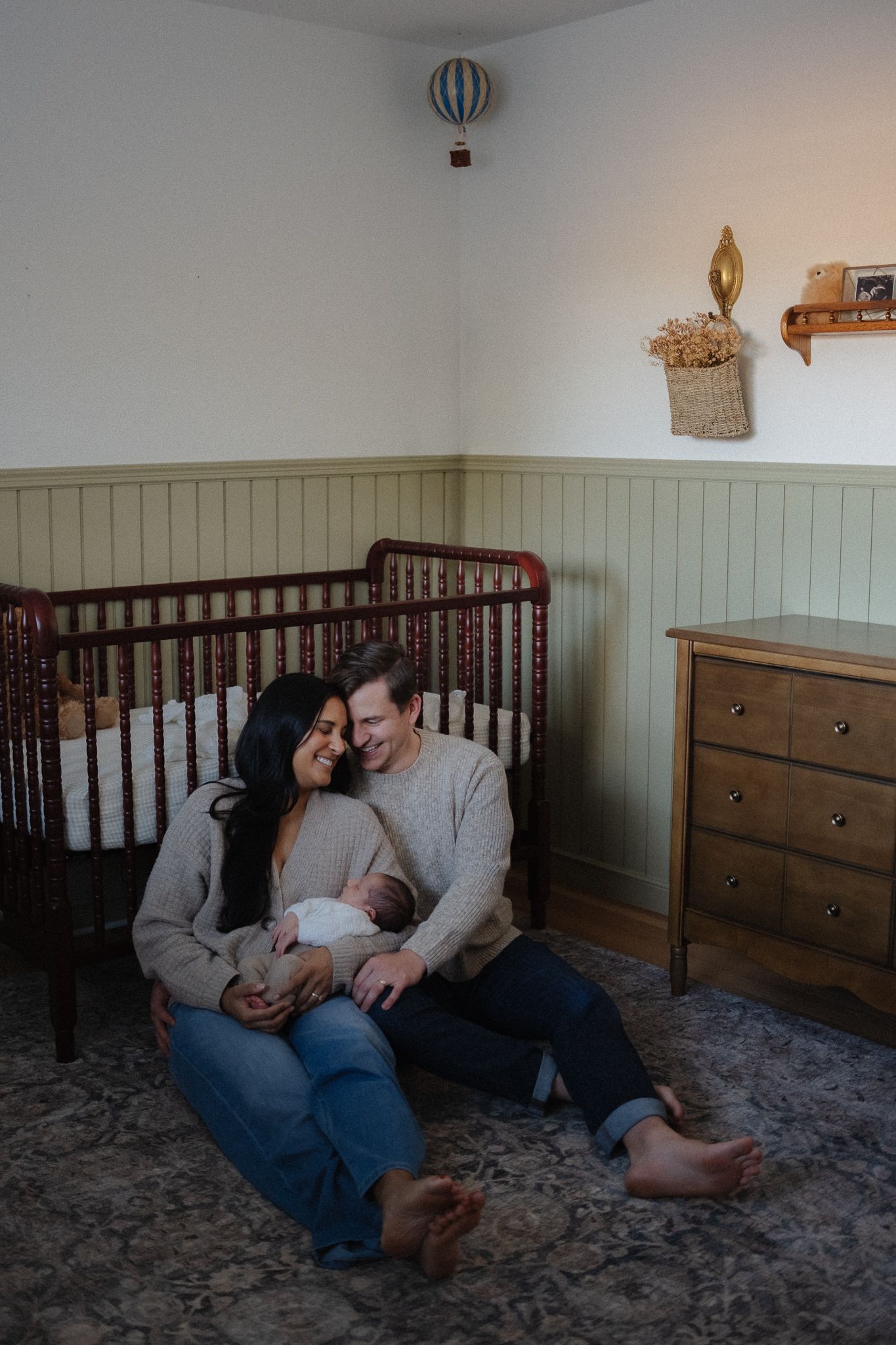 Couple relaxing together on plush carpet in a nursery room with wooden furniture and soft decor.